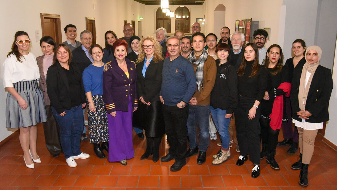 ein Gruppe sehr verschiedener Menschen stellt sich im Gang eines alten Gebäudes zum Gruppenfoto