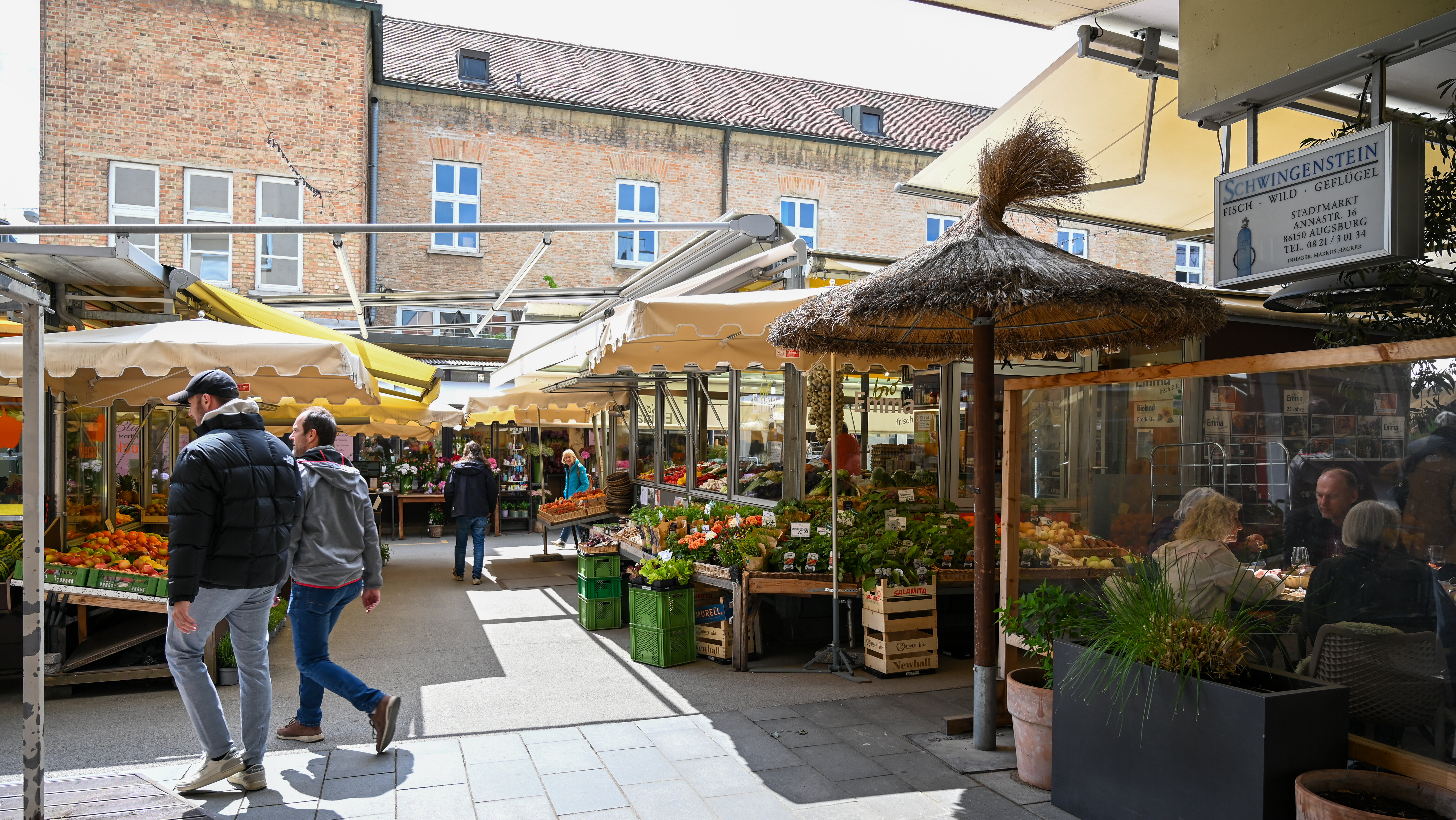 Marktgasse, rechts und links stehen Stände mit Blumen und Gemüse, im Hintergrund alte Ziegelgebäude mit Sprossenfenstern