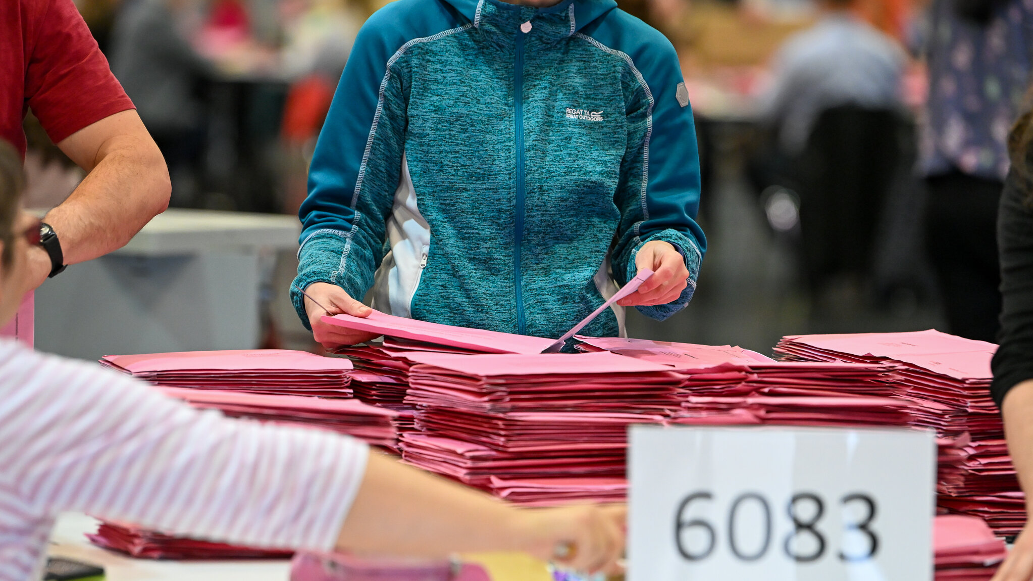 An einem Tisch werden rosafarbene Umschläge gezählt