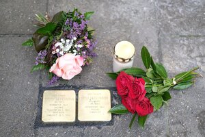 Blick von oben auf zwei Stolpersteine aus Messing; daneben Blumen und eine Kerze