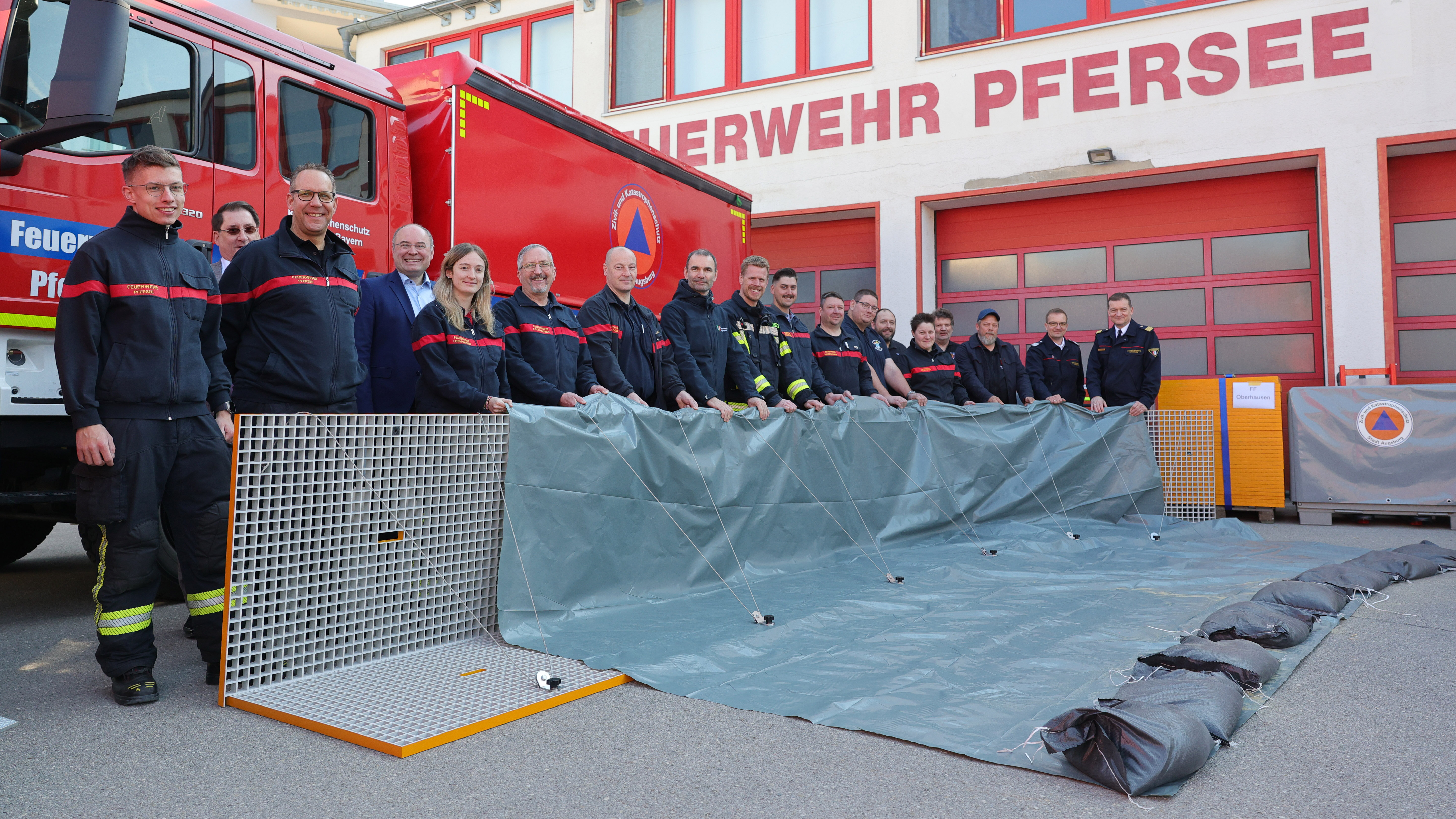 L-förmige Metall Elemente mit Folie darüber. Dahinter Feuerwehrleute.