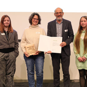 Gruppenbild von 4 menschen, die eine Urkunde halten
