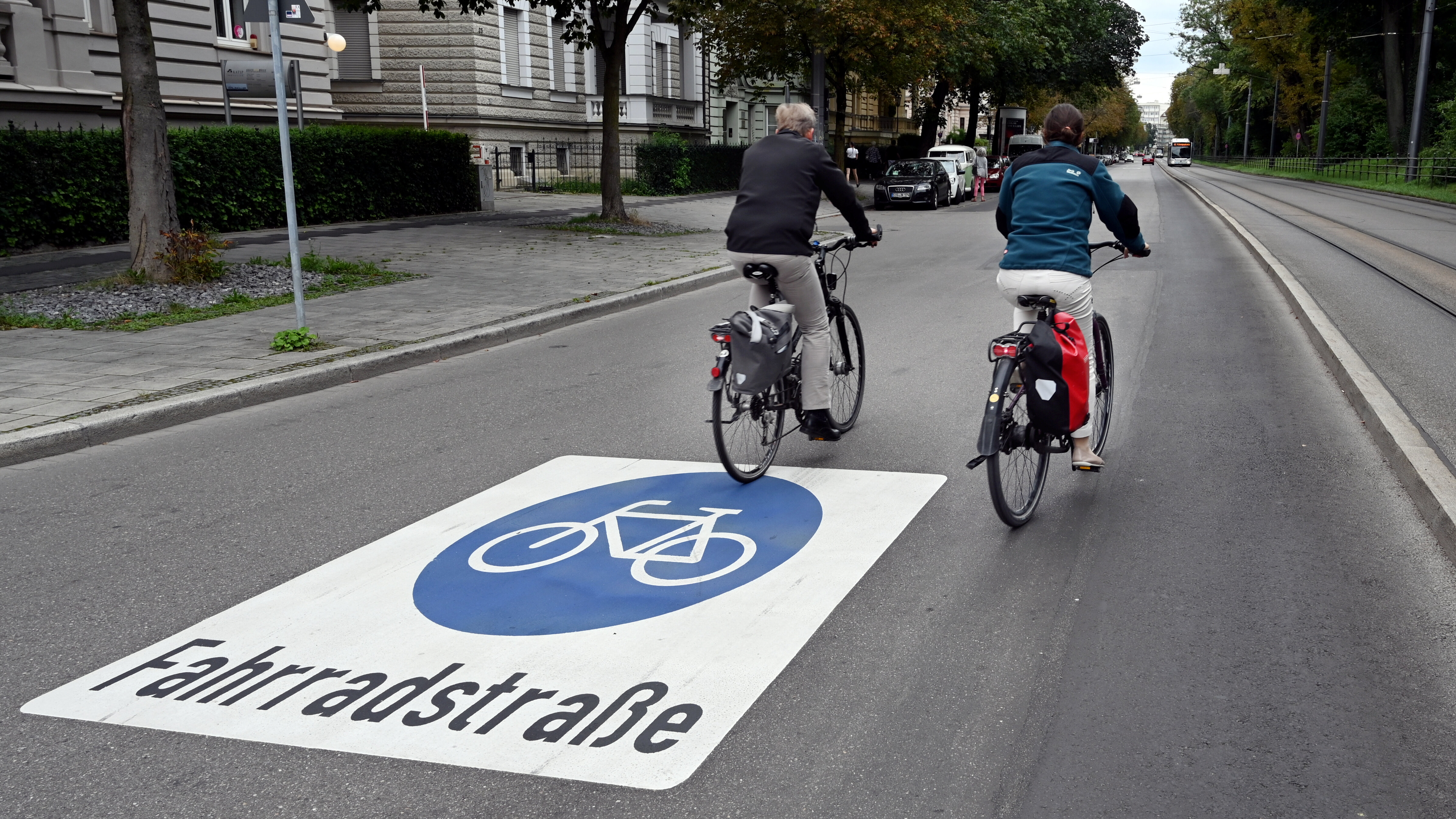 Zwei Radfahrer fahren durch eine Straße. Auf dem Boden ist die Markierung zur Fahrradstraße zu sehen