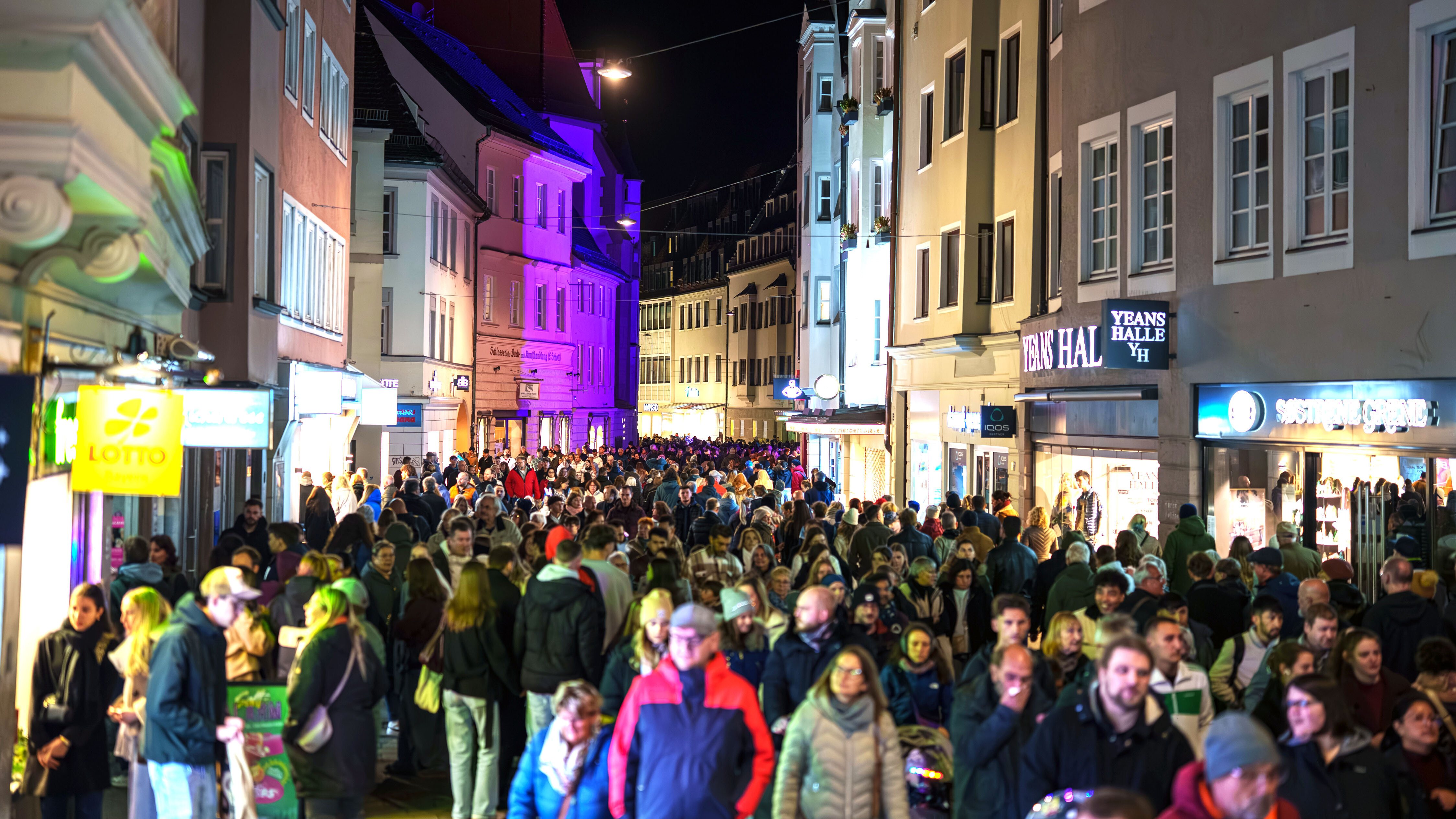 Viele Leute gehen durch die nächtliche Fußgängerzone
