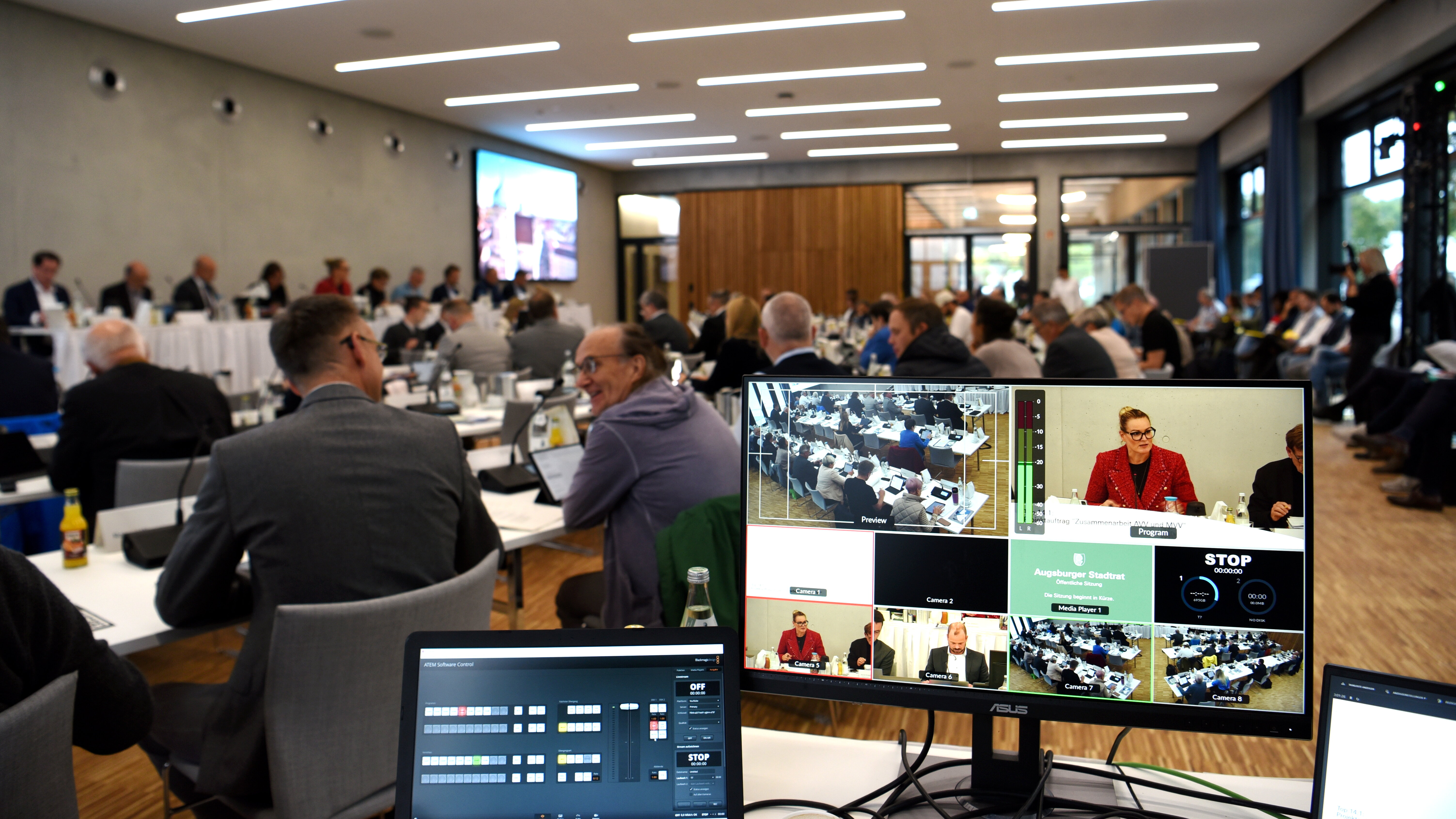 Viele Menschen sitzen in einem großen Saal. Im Vordergrund ein Bildschirm, auf dem die Aufnahmen der Sitzung zu sehen sind.