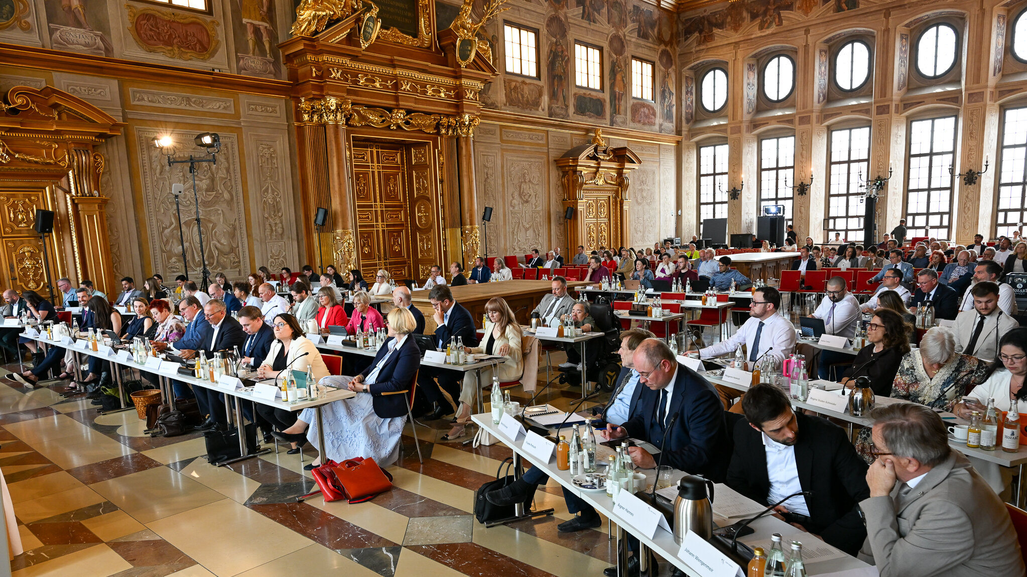 Viele Leute sitzen an langen Tischen in einem prunkvollen Saal