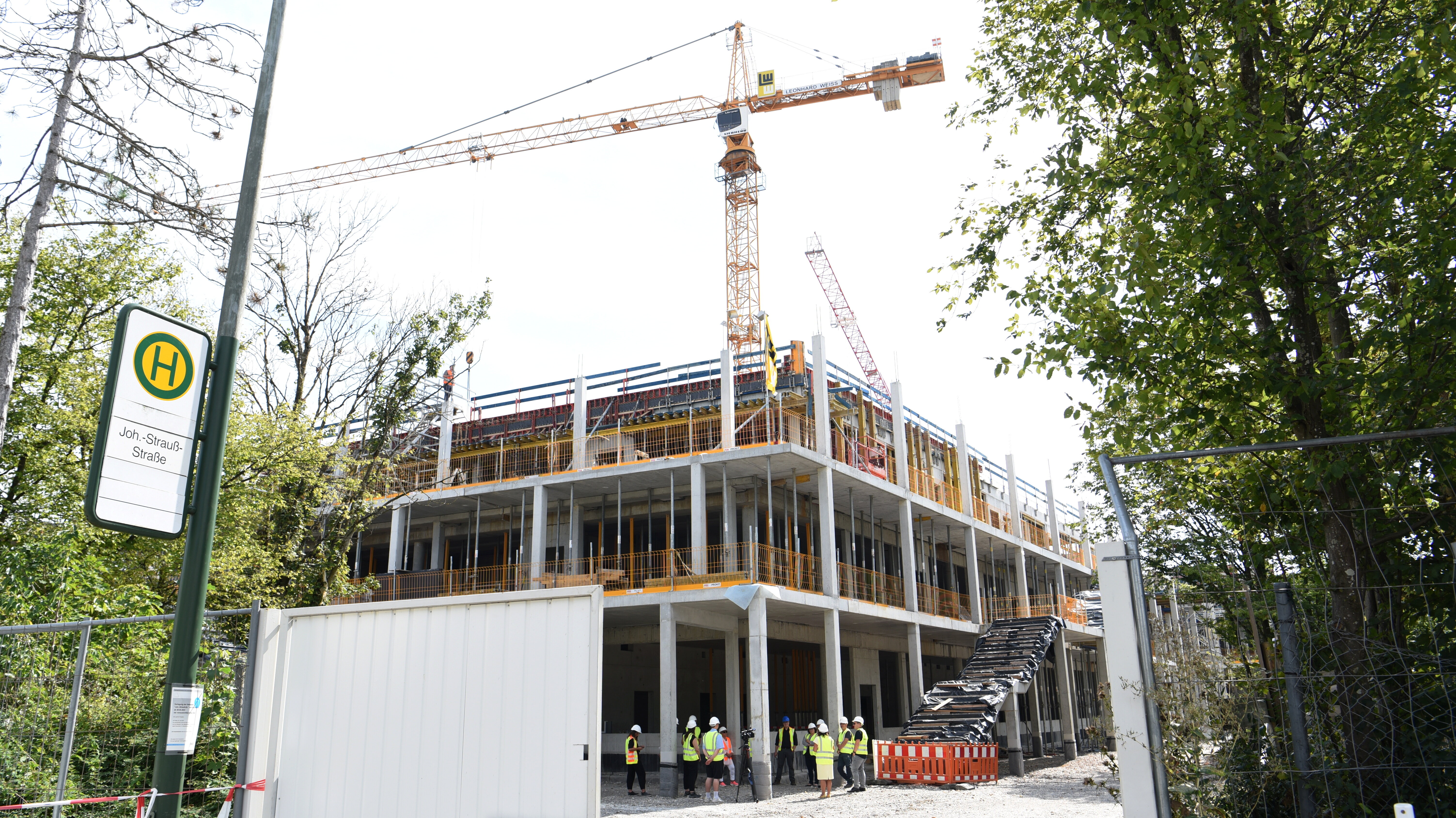 Eine Schule im Rohbau. Menschen mit Bauhelmen auf dem Kopf stehen herum. Im Hintergrund steht ein Kran