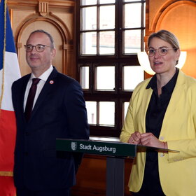 Ein Mann und eine Frau vor der deutschen und der französischen Flagge im Rathaus