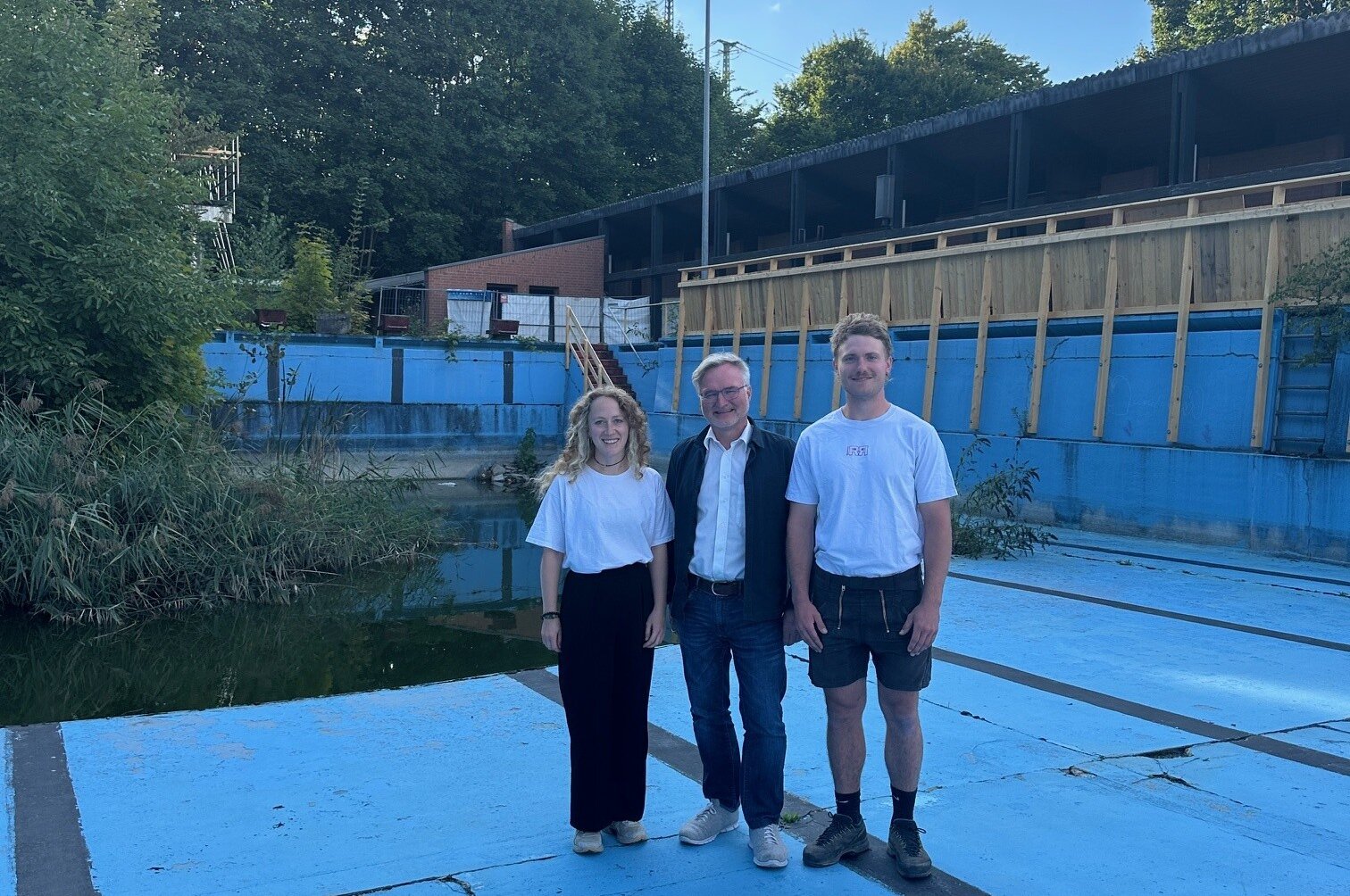 eine Frau und zwei Männer stehen in einem leeren Schwimmbecken