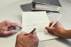 Ein Tisch auf dem ein ausgebruckter Vertrag liegt und den 2 Hände gerade unterschreiben