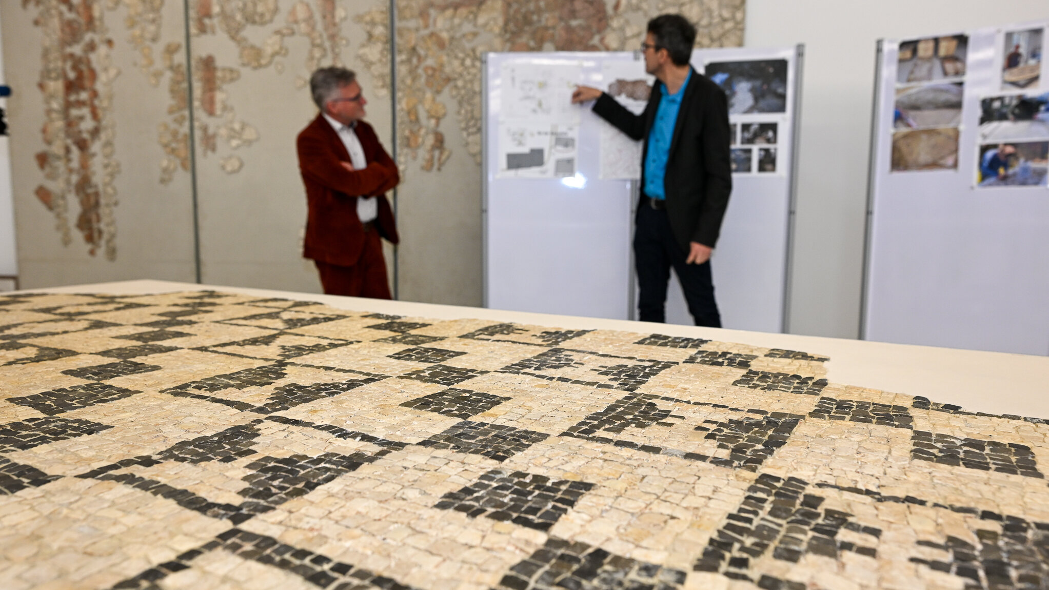 Das Foto zeigt das Römermosaik, das auf einem großen Tisch liegt.  Das Mosaik ist sschwaz weiß gemustert. Schwarze Rechtecke verlaufen dabei diagonal über weißen Grund