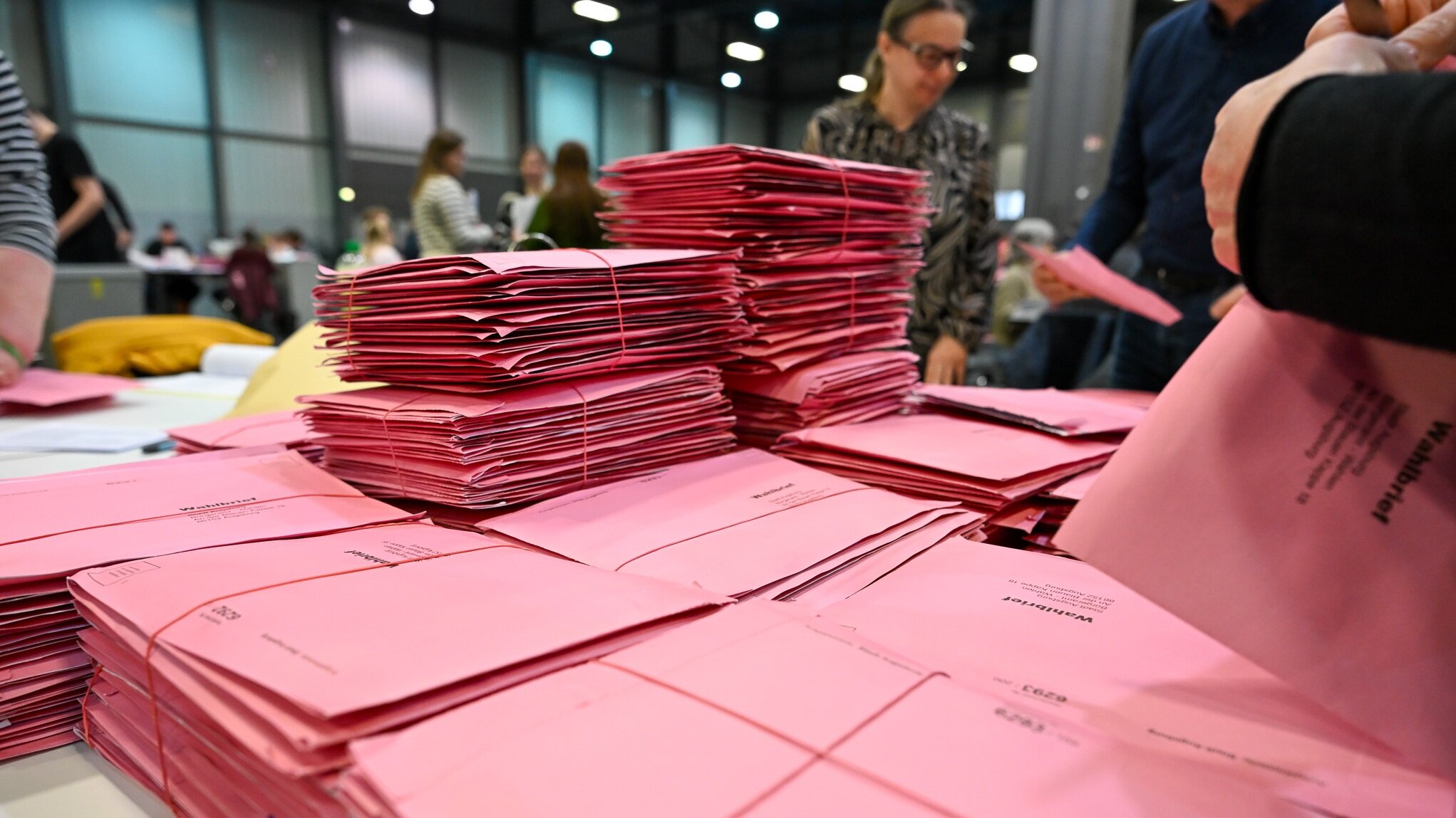 Viele Wahlbriefe liegen auf einem Tisch. Dahinter stehen Leute, die die Briefe öffnen
