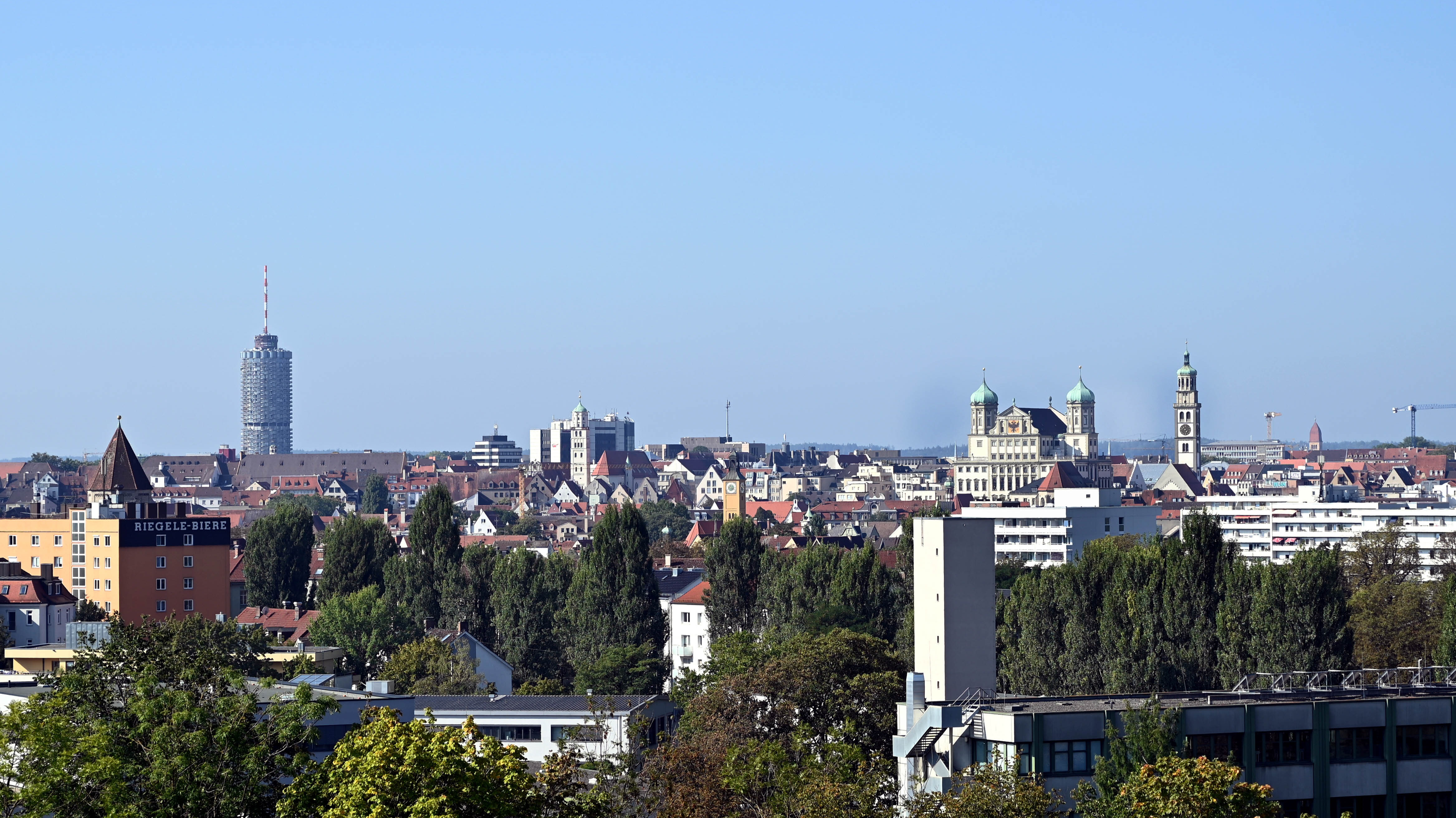 Blick über die Dächer von Augsburg Richtung Hotelturm und Rathaus; es ist leicht diesig bei blauem Himmel