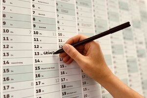 eine Hand trägt grade mit einem Stift einen Termin in einen Wandkalender ein