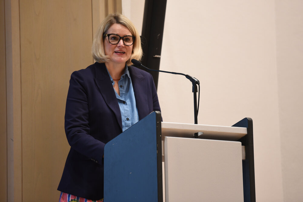 blonde Frau mit Brille und Blazer am Rednerpult