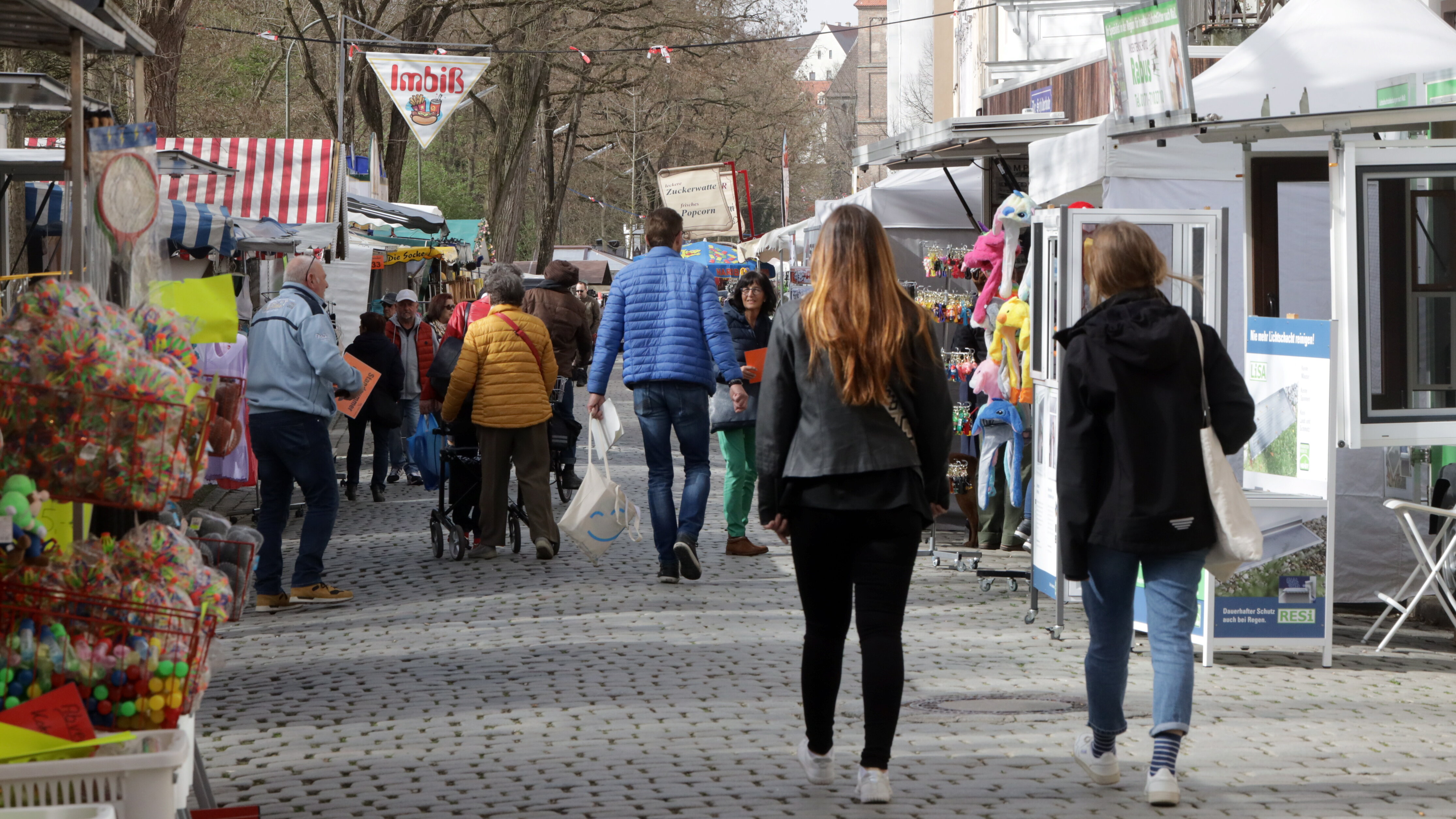 eine Marktstraße mit Ständen auf beiden Seiten, darunter Blumen, ein Imbiss, ein Infopavillon