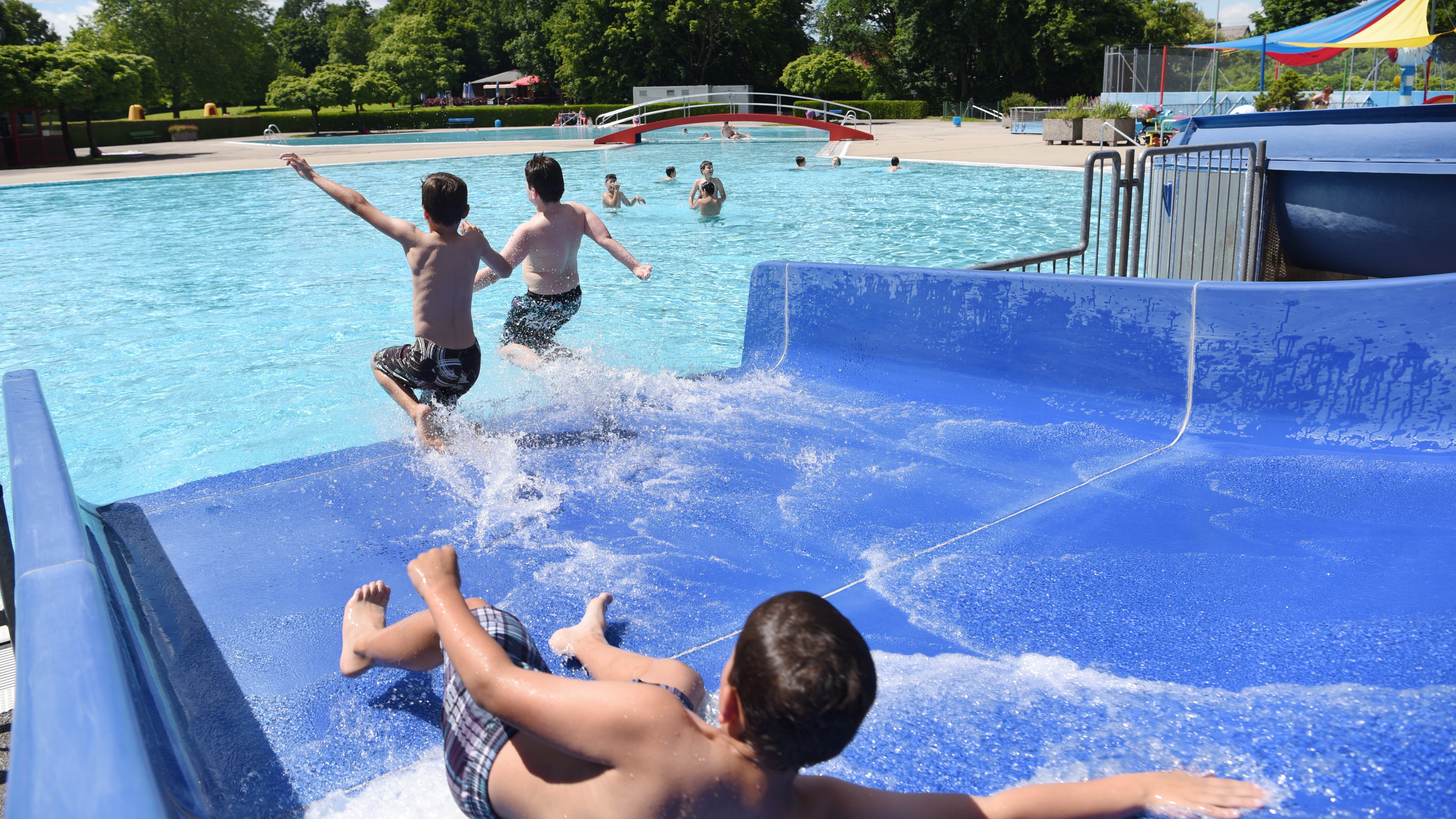 Drei Kinder auf einer Wasserrutsche in einem Schwimmbad.