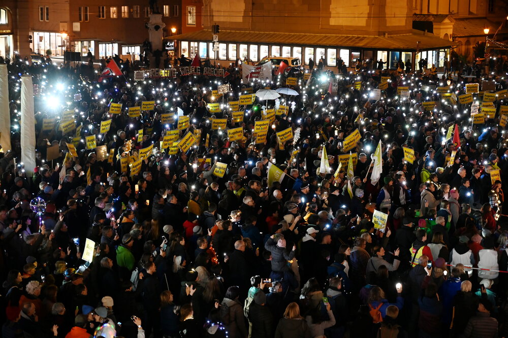 Auf dem Rathausplatz stehen mehrere Tausend Menschen bei Dunkelheit und halten Lichter in die Höhe