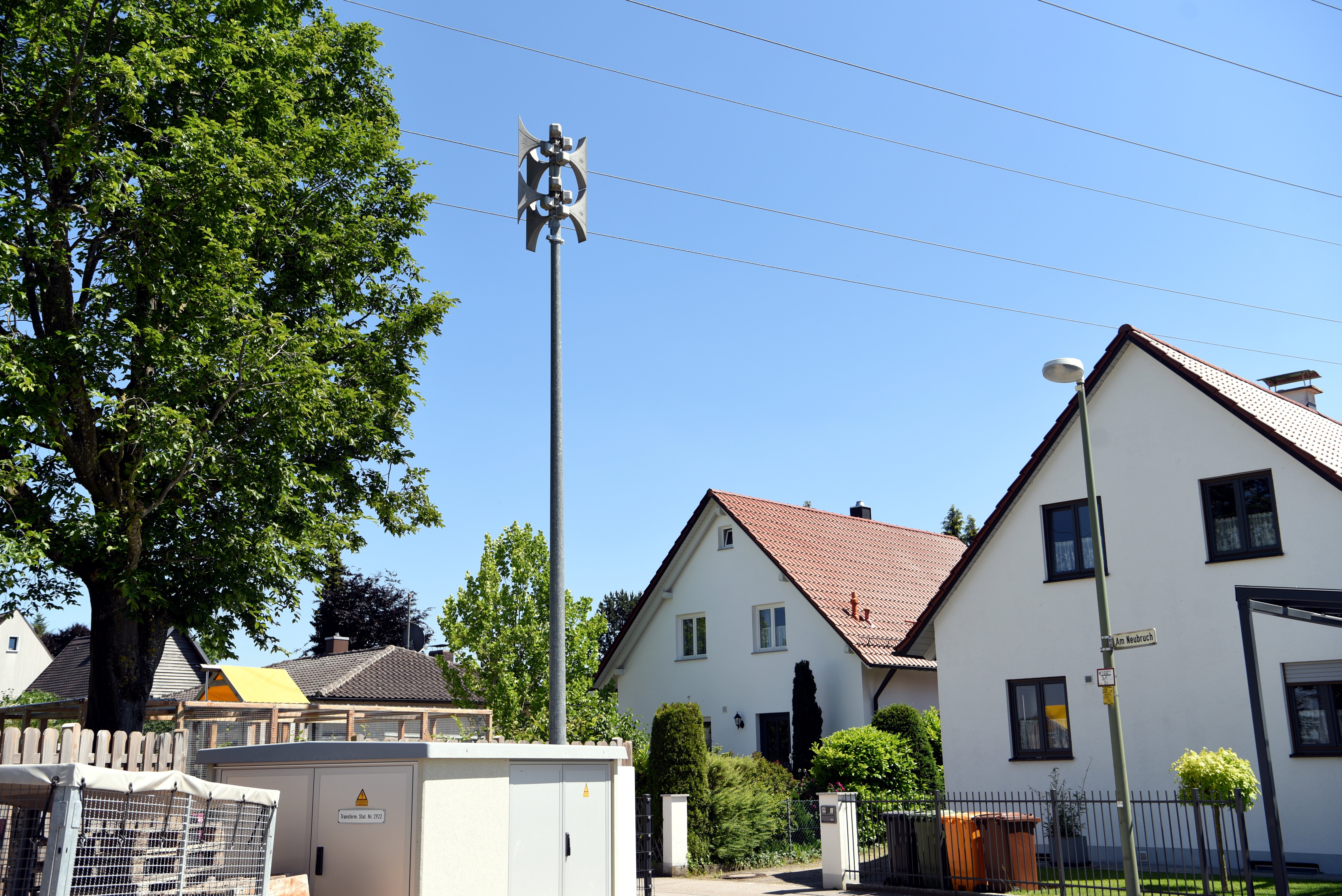Auf einem Mast steht eine Sirene. Im Hintergrund sind Häuser und Bäume zu sehen