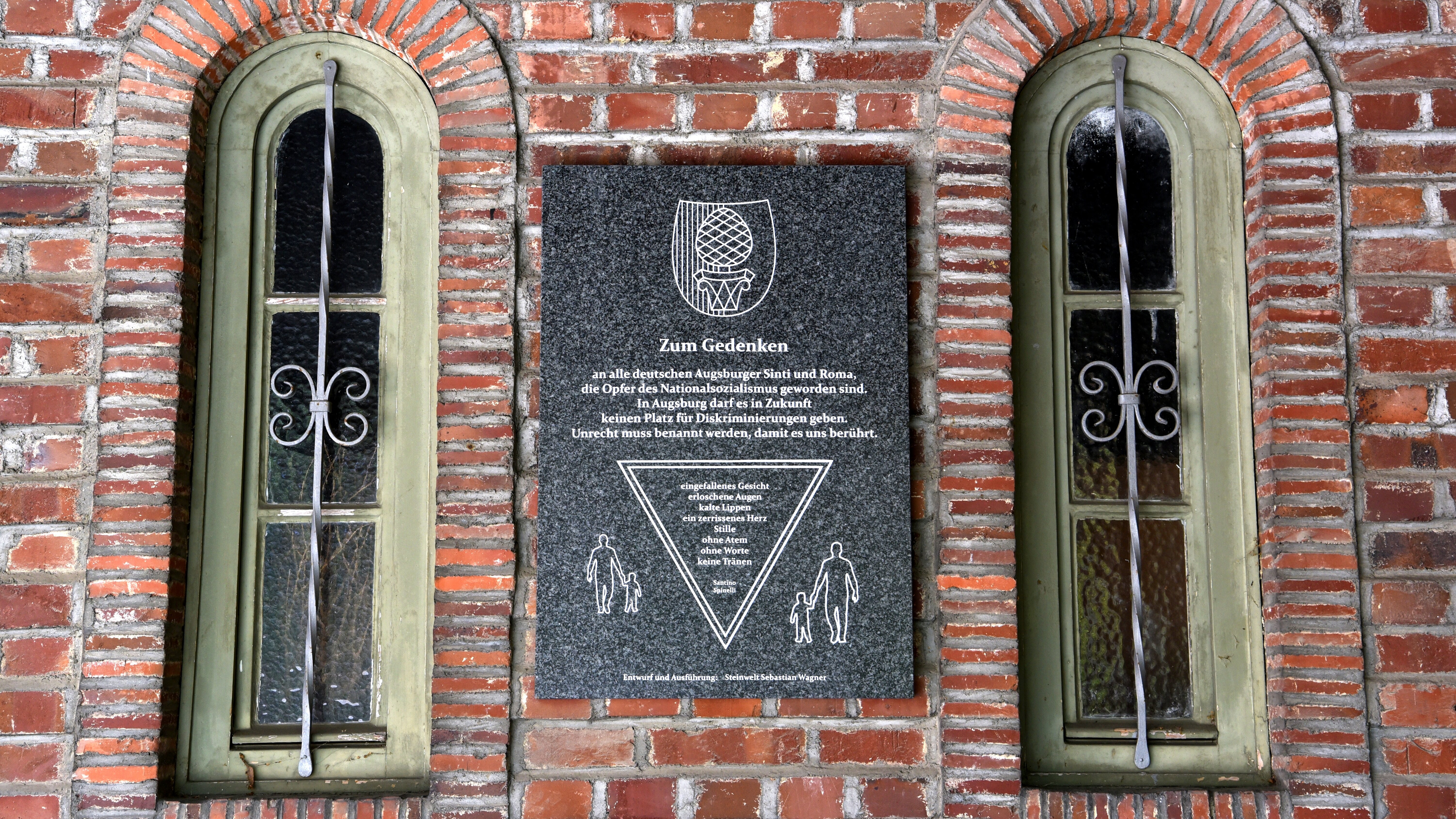 Gedenktafel zwischen zwei Fenstern an Backsteingebäude
