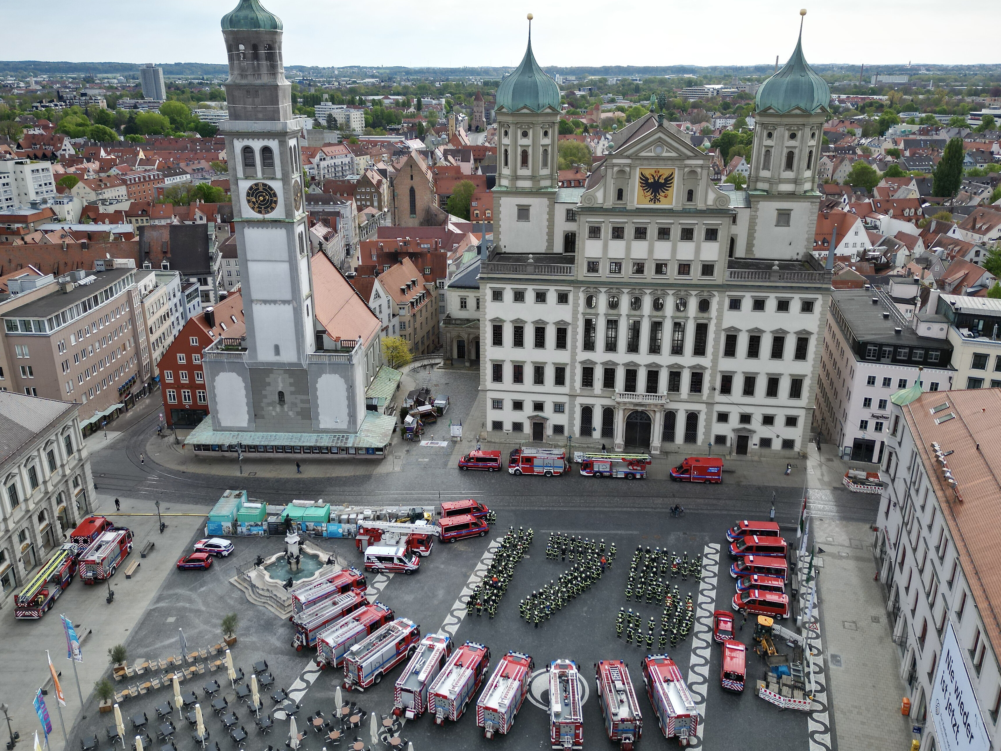 Ein Foto von oben auf den Rathausplatz. Dort stehen Feuerwehrmänner und-frauen, die die Zahl 175 bilden, sowie Löschfahrzeuge.