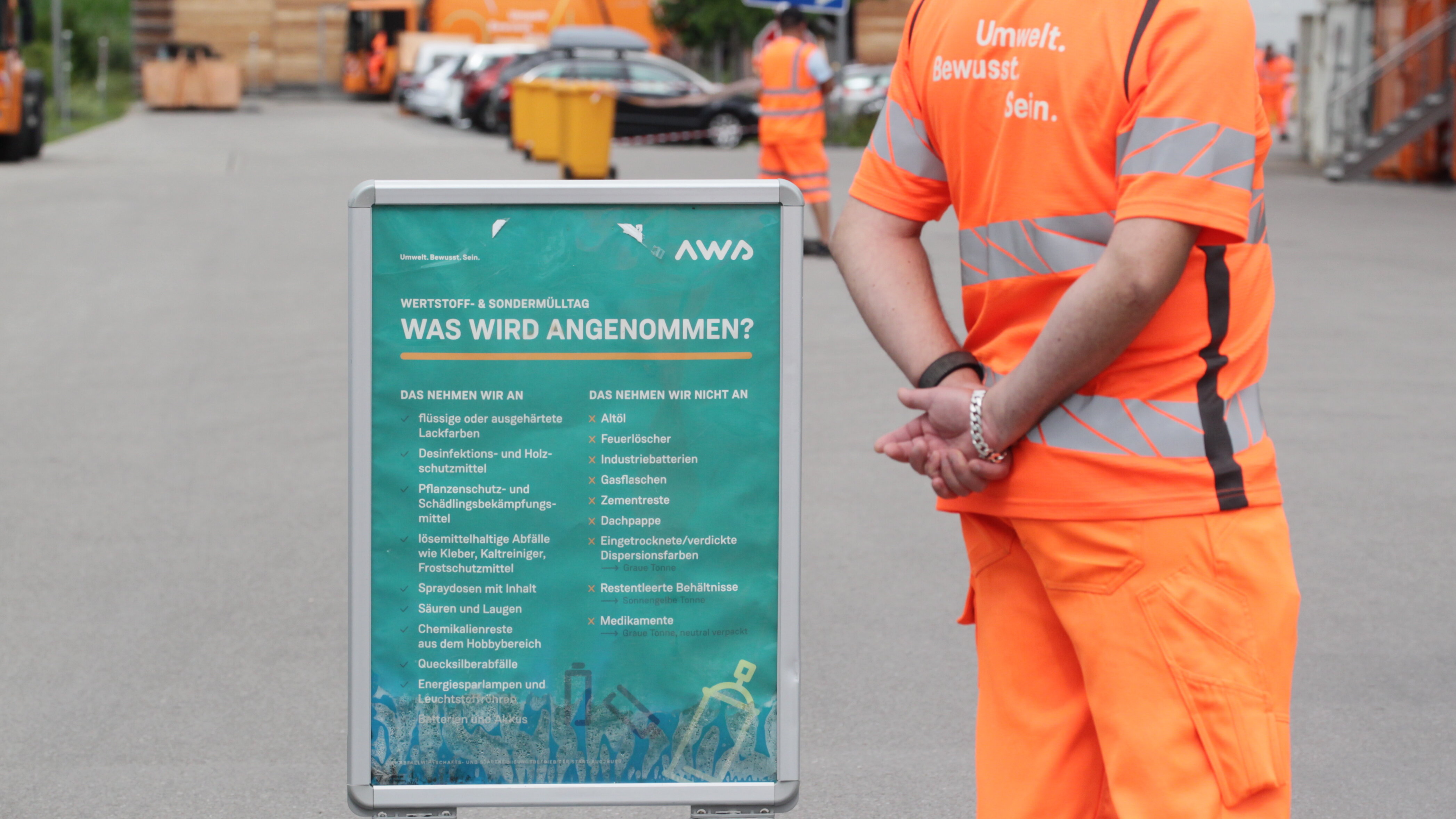 Mann in oranger Berufskleidung steht neben einem Schild, auf dem der AWS aufgelistet hat, was angenommen wird