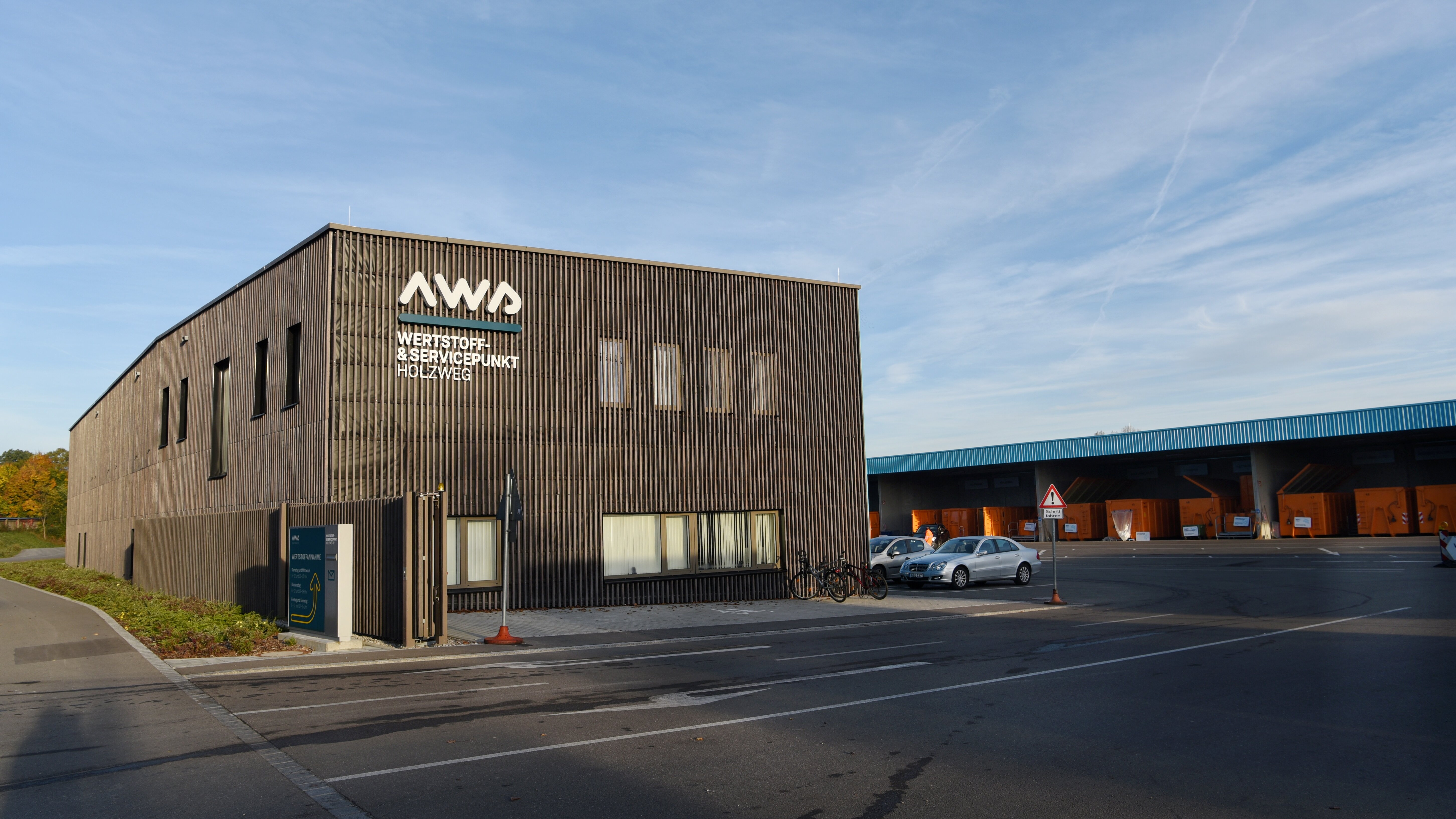holzverkleidetes Gebäude mit Flachdach, an der Fassade "AWS Wertstoff- und Servicepunkt Holzweg"