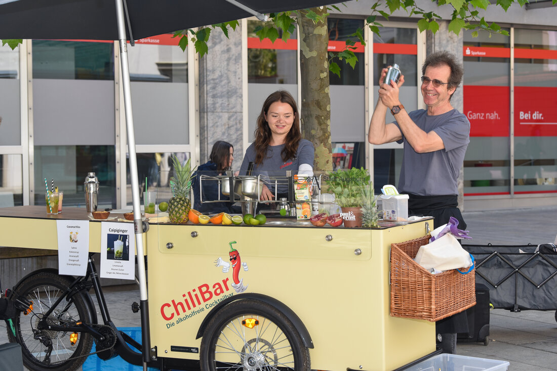 ein Mann und eine Frau stehen hinter einem Lastenfahrrad, das zur Bar ausgebaut ist, und mixen Cocktails