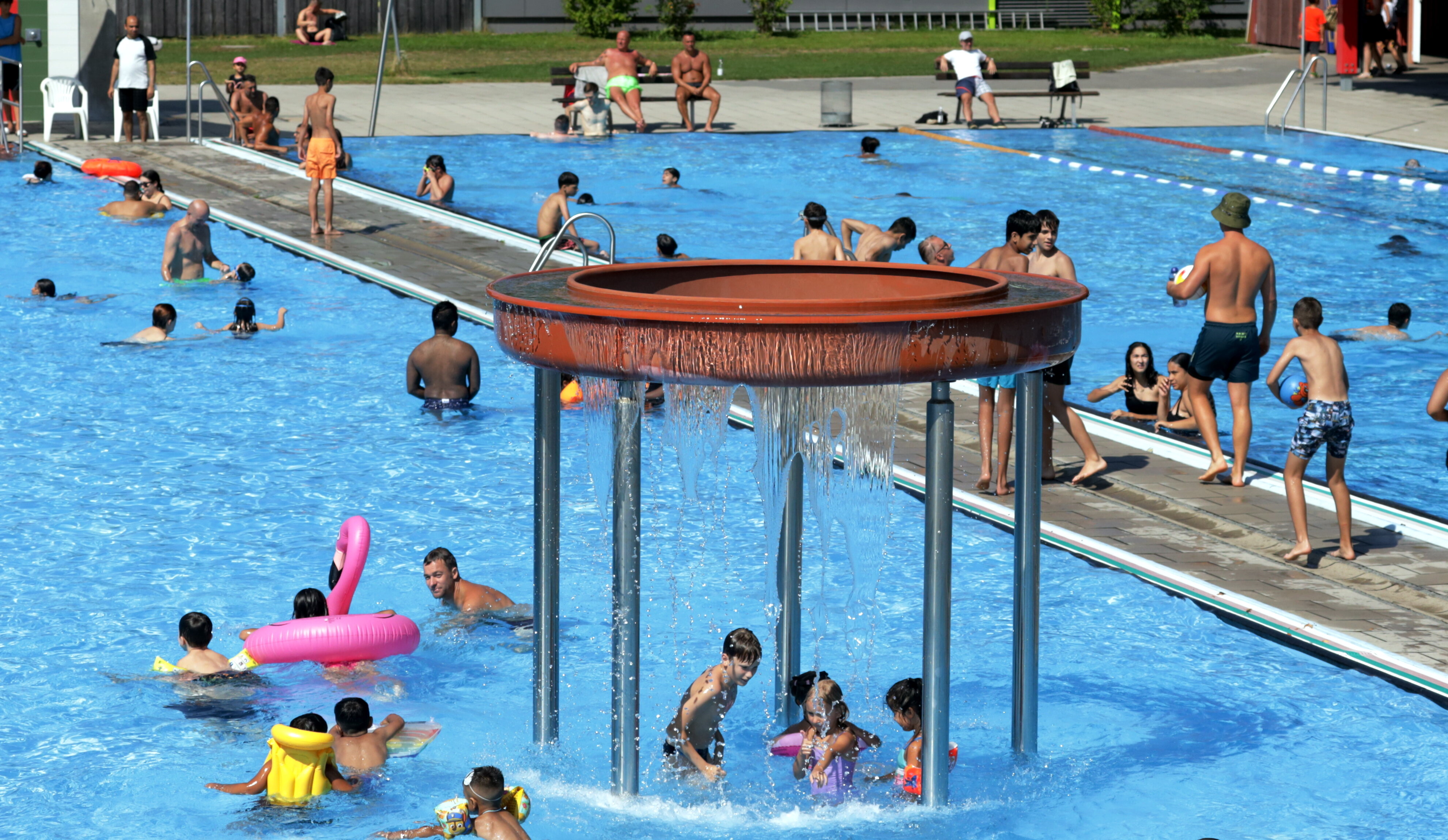 Im Familienbad herrscht buntes Treiben im Nichtschwimmerbecken. Dazu lacht die Sonne und der himmel ist blau.