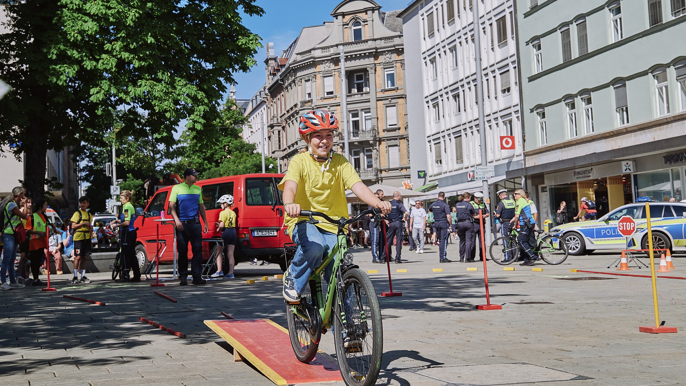 Das Bild zeigt, wie ein Mädchen mit seinem Fahrrad über eine flach Holzwippe balanciert 