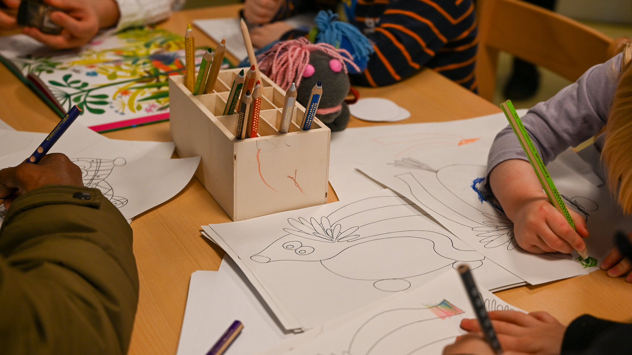 An einem Tisch malen Kinder Bilder mit Buntstiften