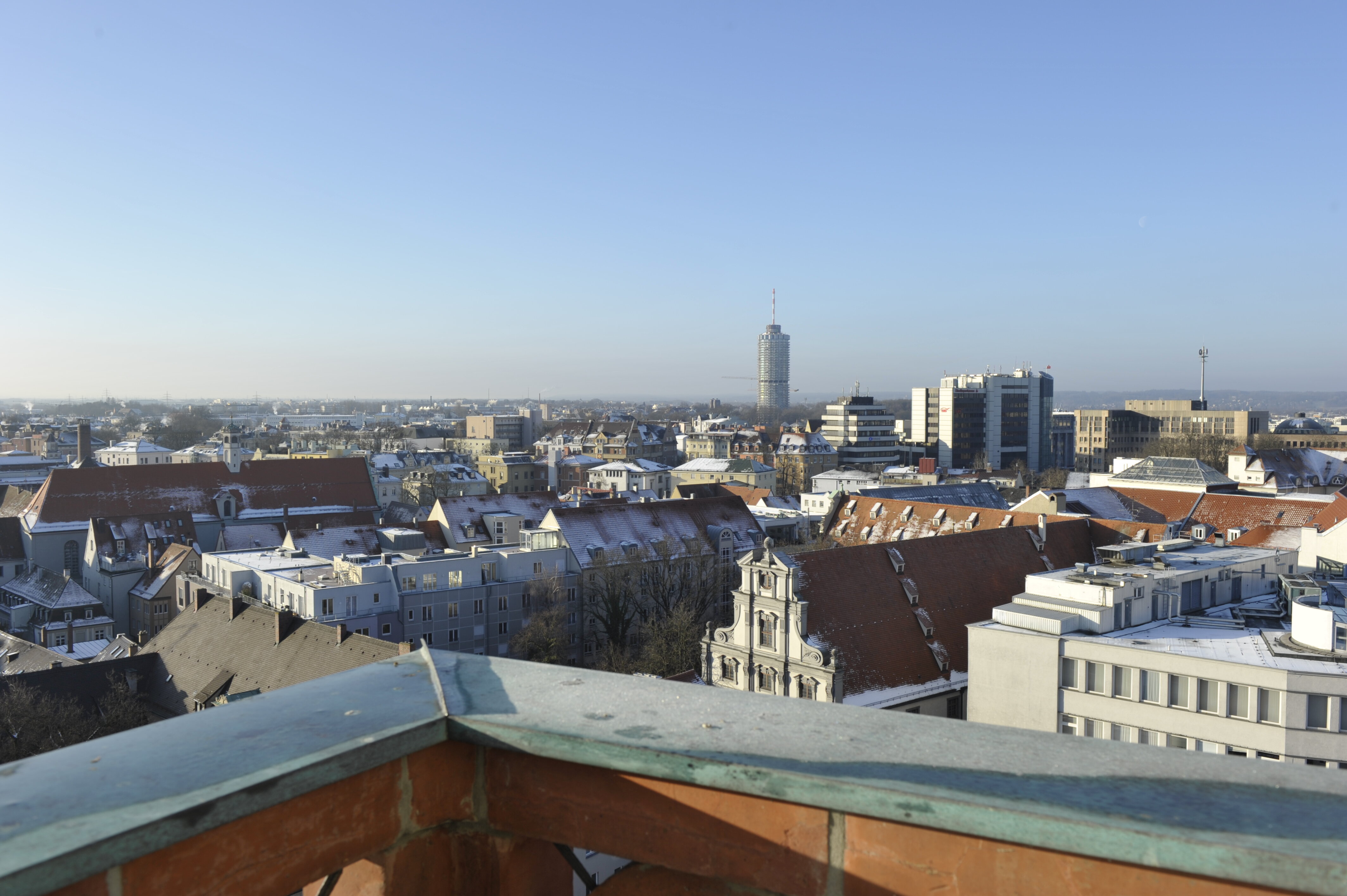 Blick über die Dächer von Augsburg Richtung Hotelturm; es ist leicht diesig bei blauem Himmel