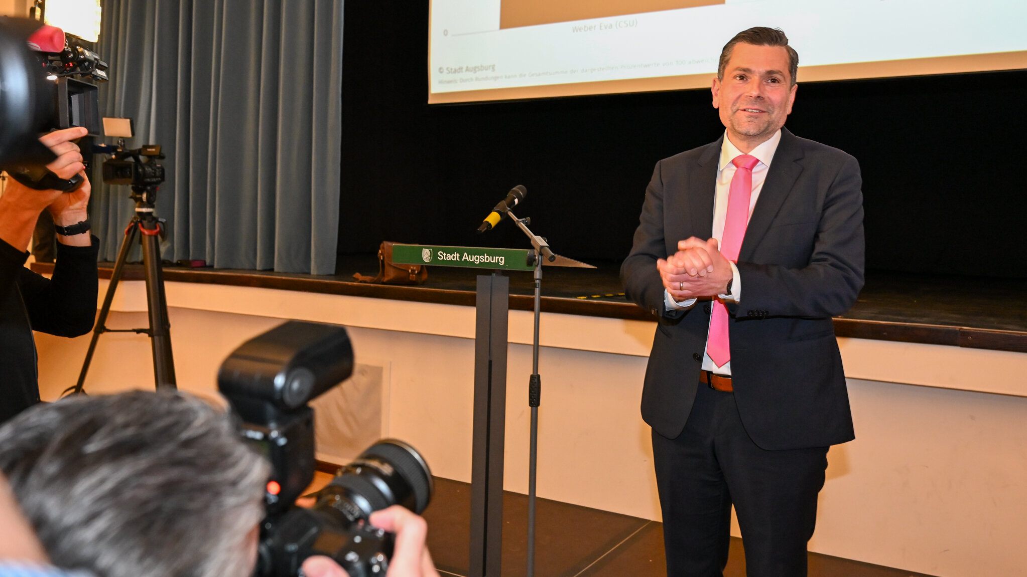 Ein Mann im Anzug steht an einem Rednerpult. Vor ihm sind Fotografen