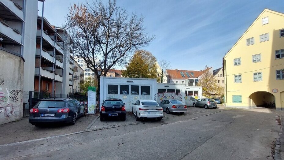 Das Foto zeigt eine Asphaltfläche. Auf dieser stehen mehrere Garagen, vor denen Autos stehen. Auf den Garagen und einer Hauswand ist viel Graffiti gesprüht.