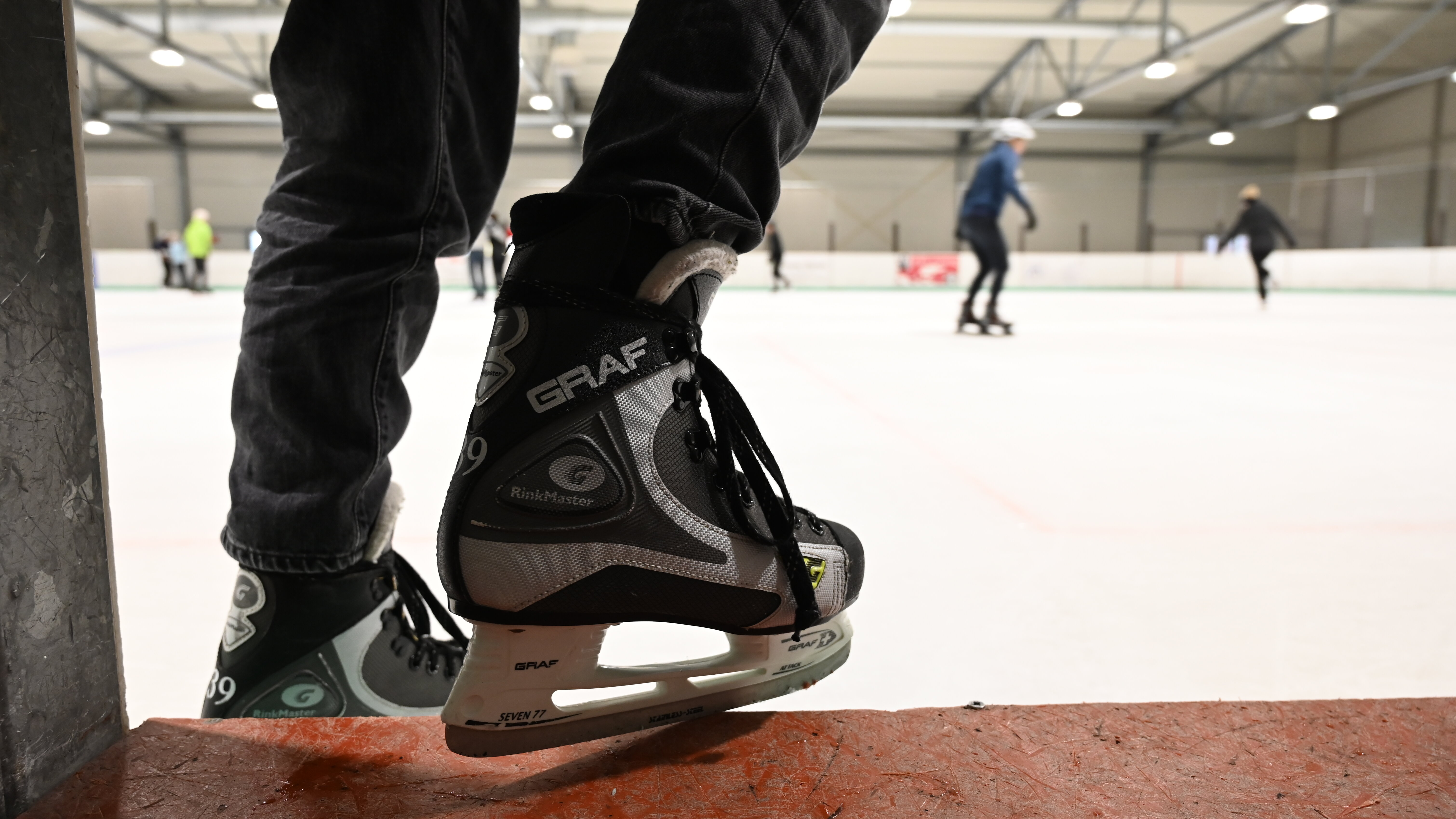Schlittschuhe im Vordergrund. Eishalle mit Schlittschufahrenden im Hintergrund