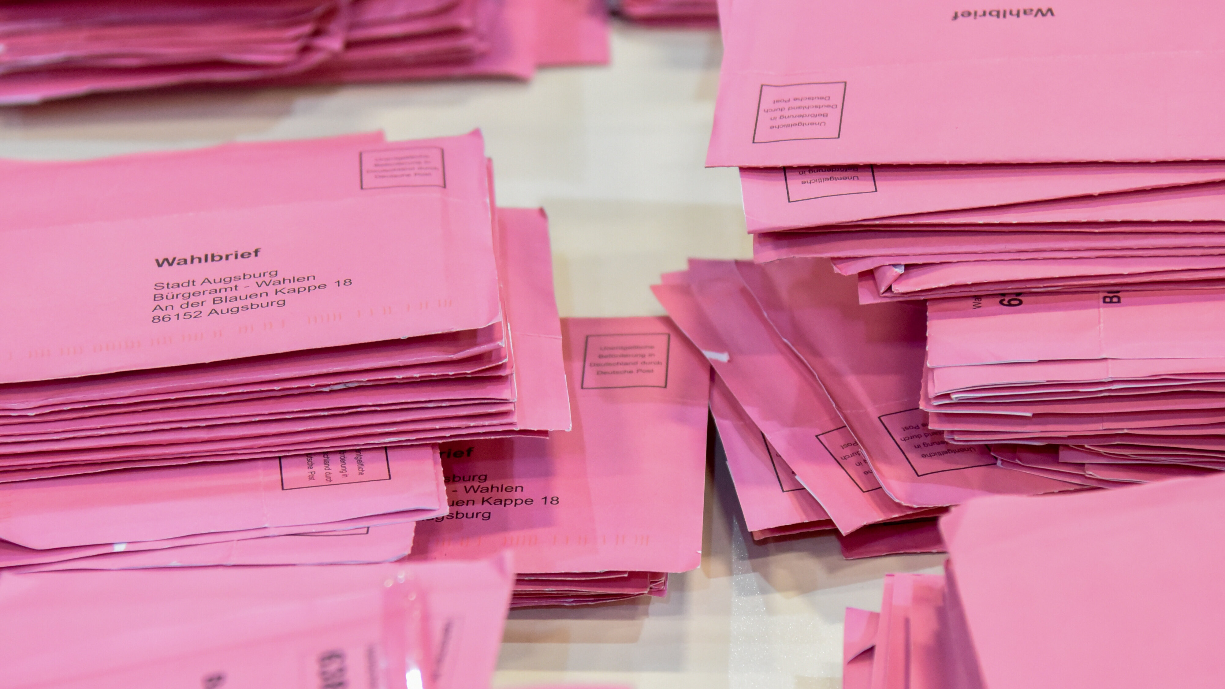 Stapelweise rosafarbene Briefkuverts auf einem Tisch.
