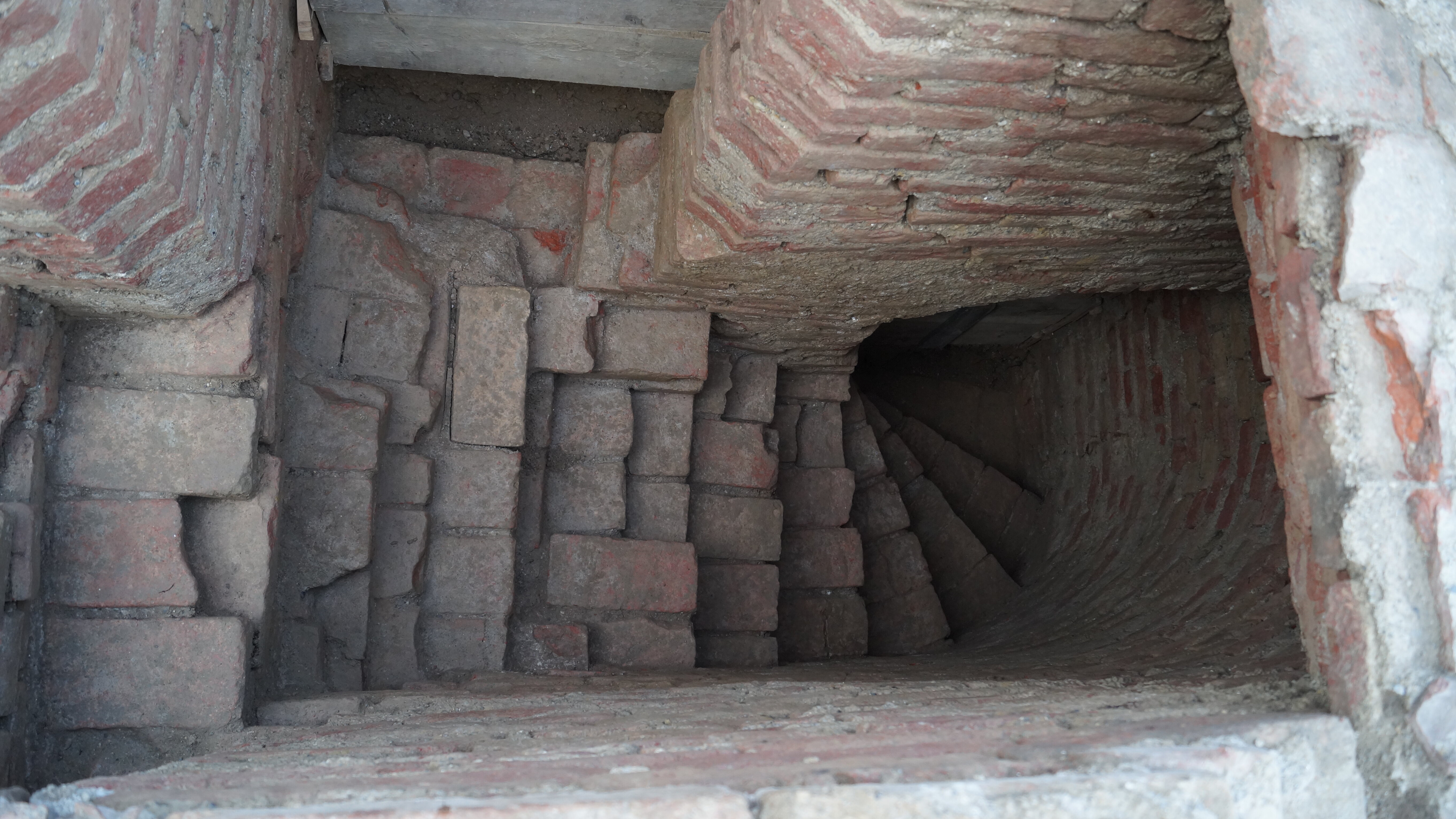 Blick von oben einen Treppe hinuntzer, das Bauwerk ist aus Ziegeln errichtet und ersichtlich sehr alt.