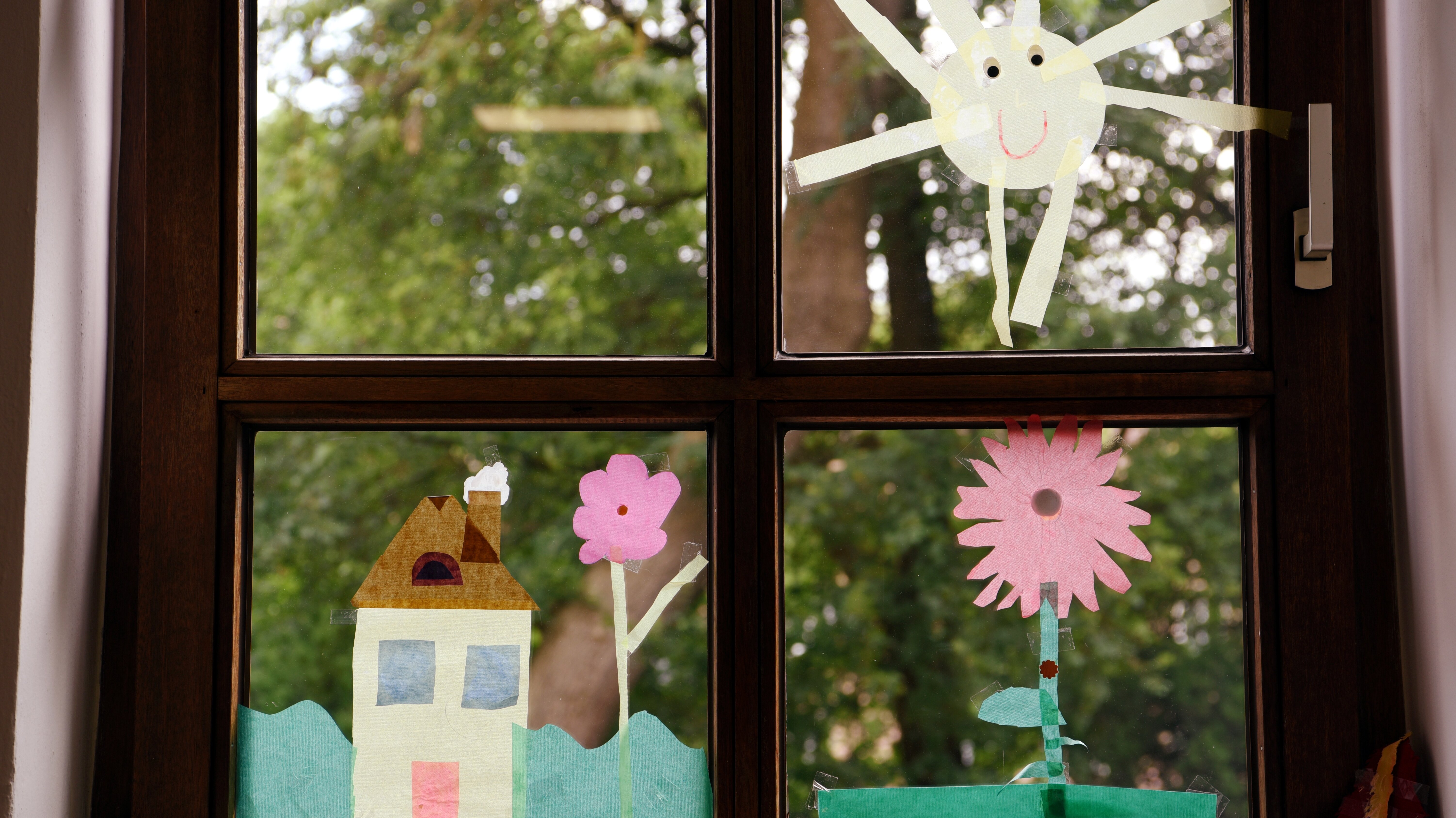 Ein Fenster zum Garten. Auf den Scheiben sind Blumen, ein Haus und eine Sonne aus buntem Papier aufgeklebt