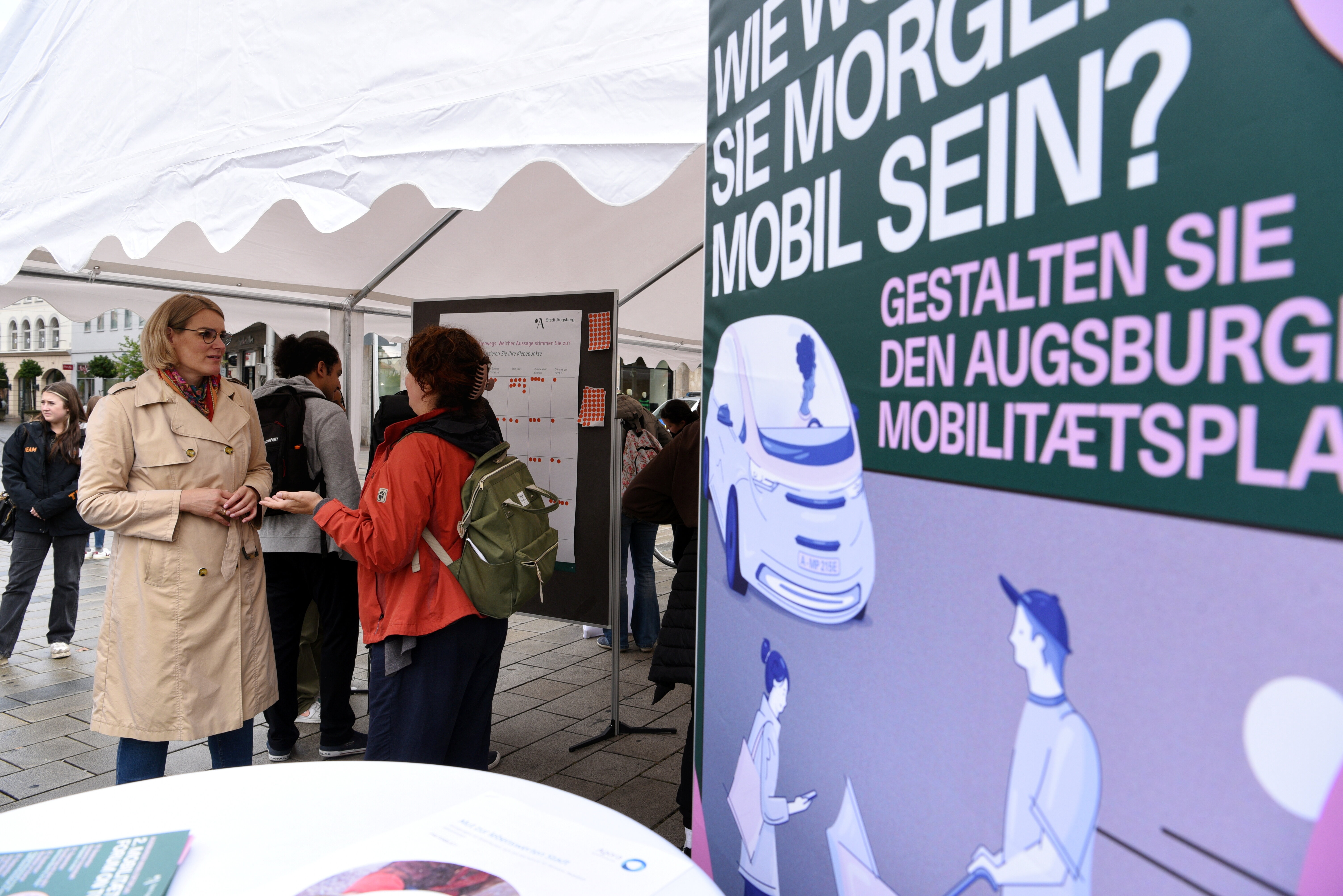 Oberbürgermeisterin Eva Weber unterhält sich mit einer Bürgerin. Rechts ist ein Plakat zu sehen, das auf den Mobilitätsplan hinweist.