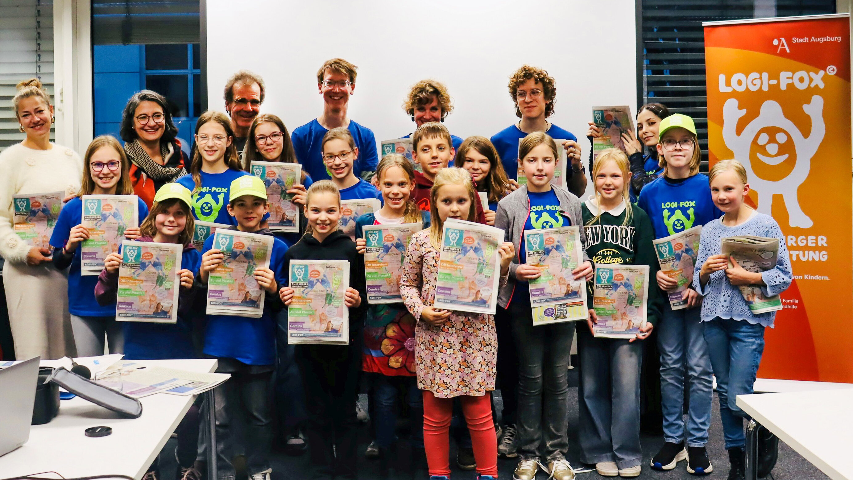 Etwa 15 Kinder und ein paar Erwachsene. Jeder hält eine Ausgabe der Kinderzeitung in der Hand