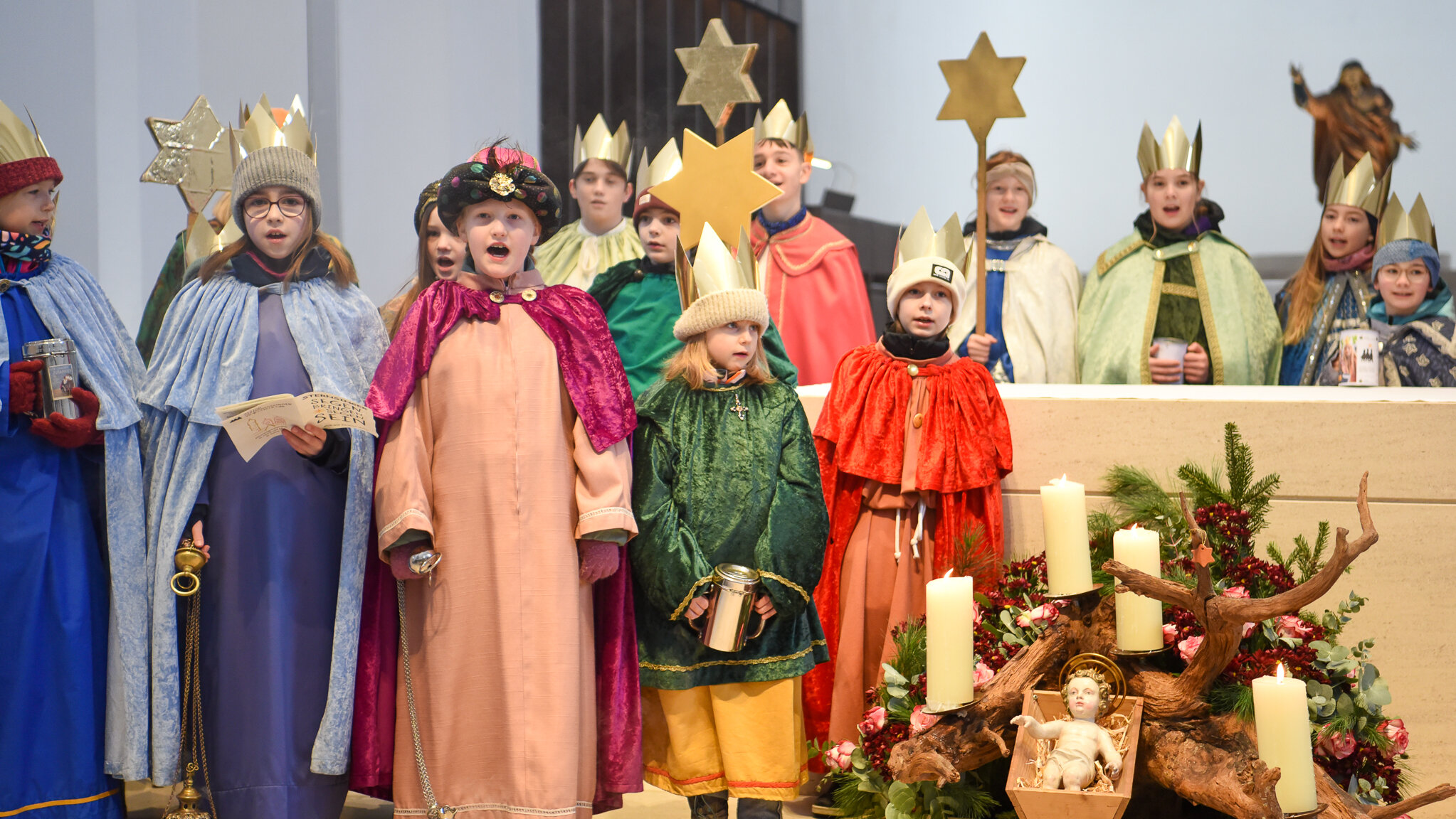 Kinder verkleidet als die Heiligen Drei Könige stehen in einer Kirche. Neben ihnen ist eine Krippe aufgebaut.