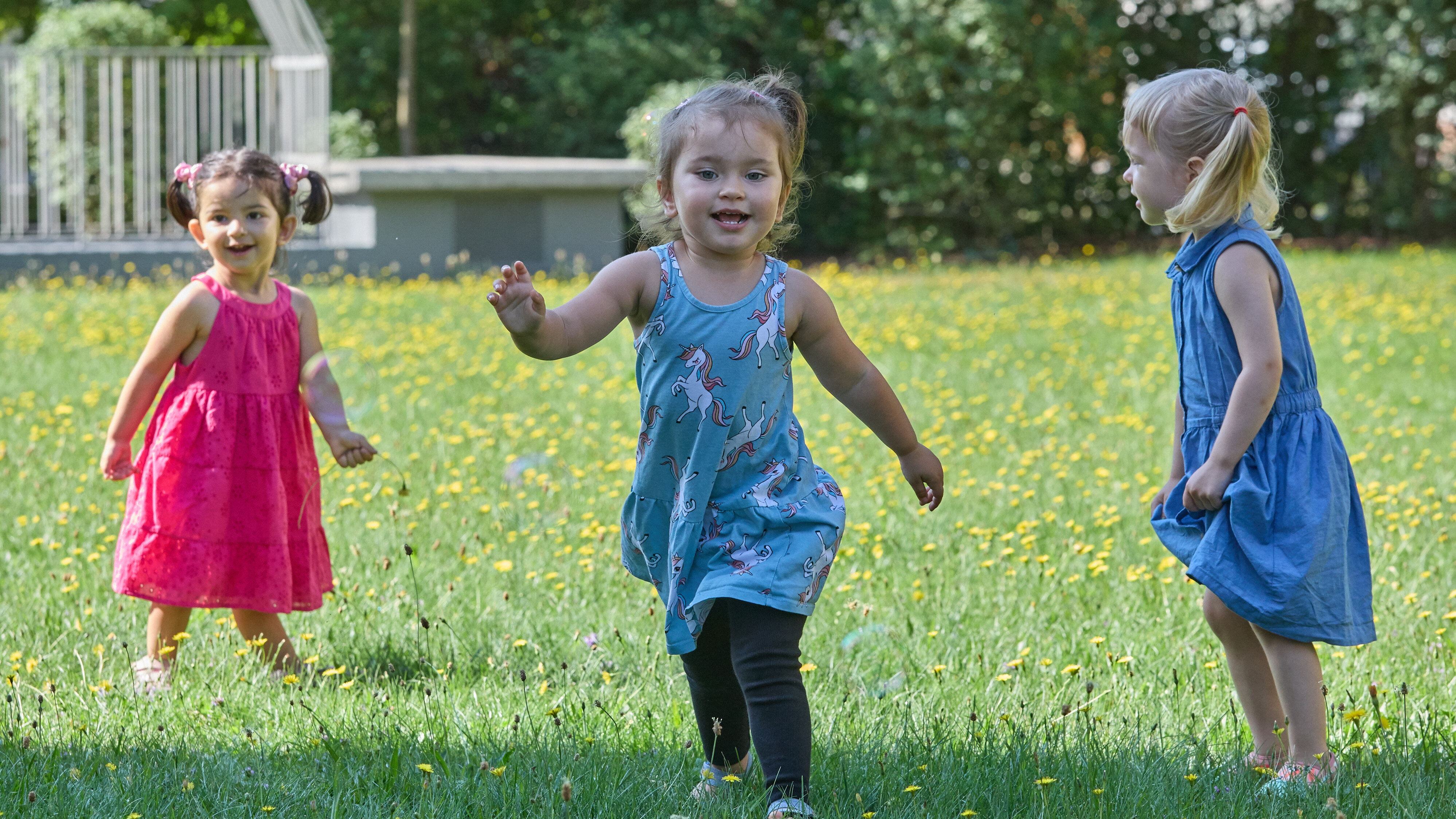 drei Kinder spielen auf grünem Rasen im Sonnenschein