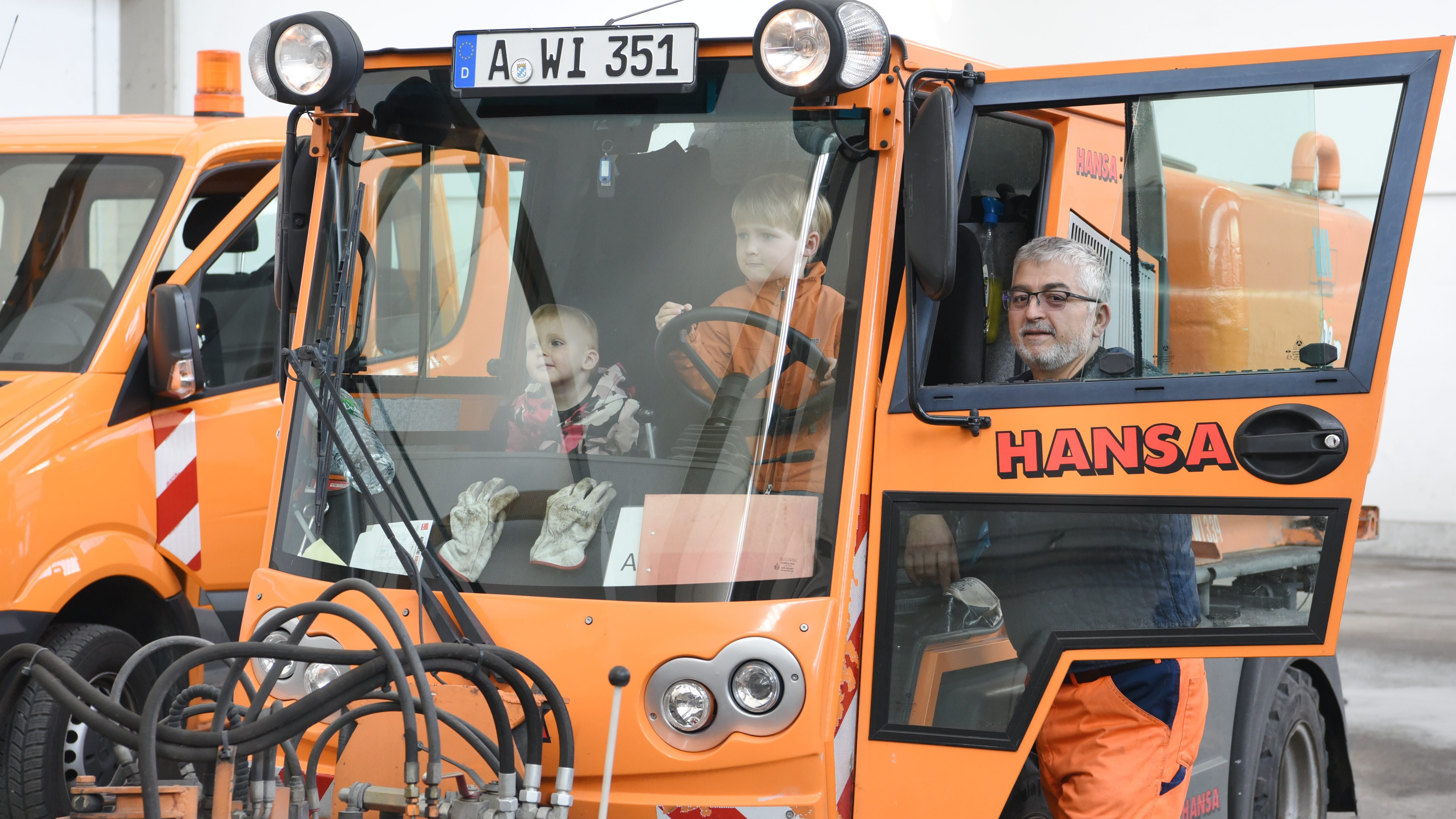Zwei Kinder sitzen in einem Fahrzeug der Müllabfuhr. Ein Mitarbeiter erklärt ihnen etwas. 
