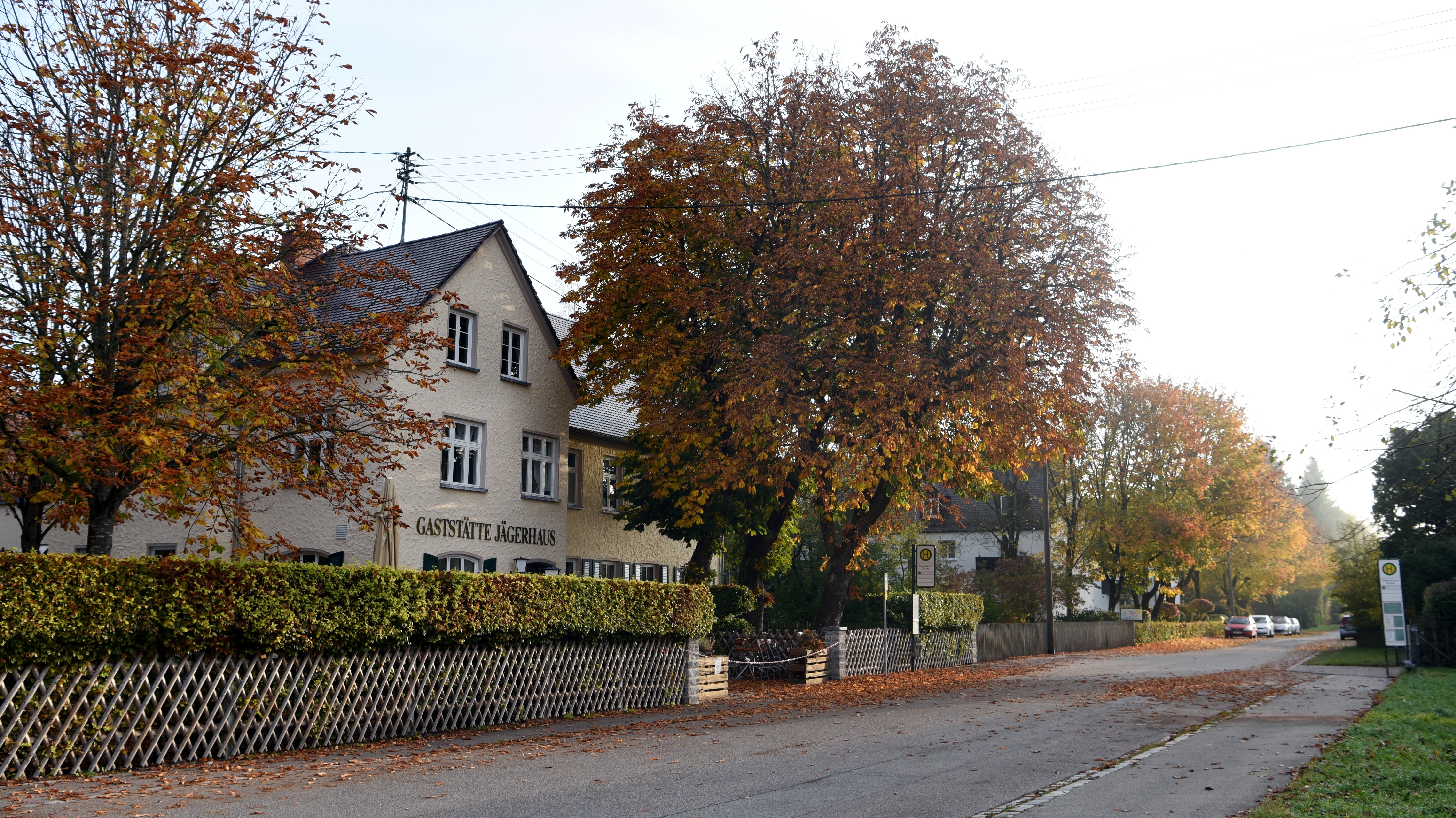 Das Foto zeigt den Stadtteil Siebenbrunn. Darauf sieht man eine Straße ohne Autos ein Haus auf dem Gaststätte Jägerhaus steht, neben dem zwei Bäume stehen.