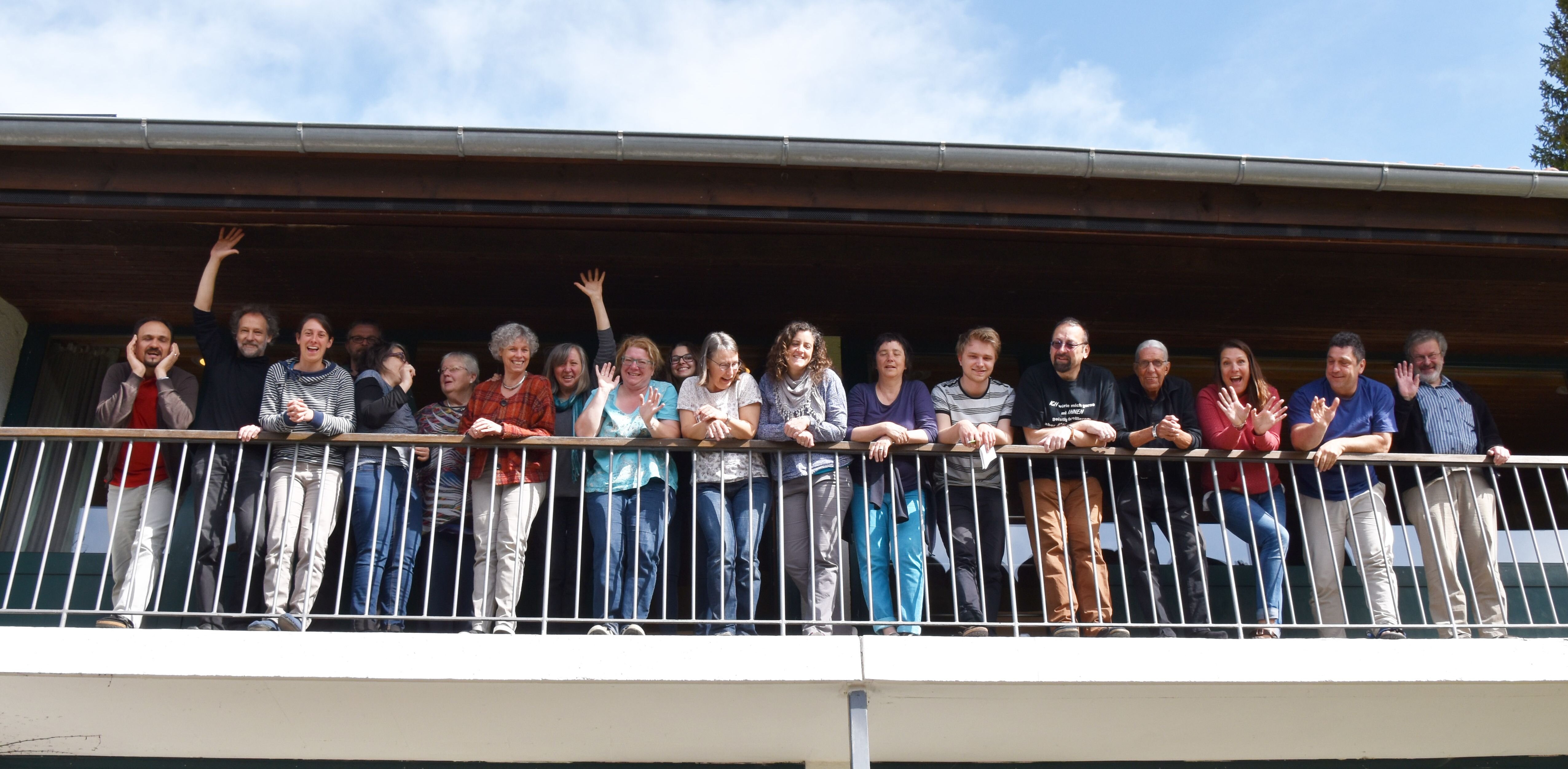 Männer und Frauen stehen nebeneinander am Geländer eines langen Balkons