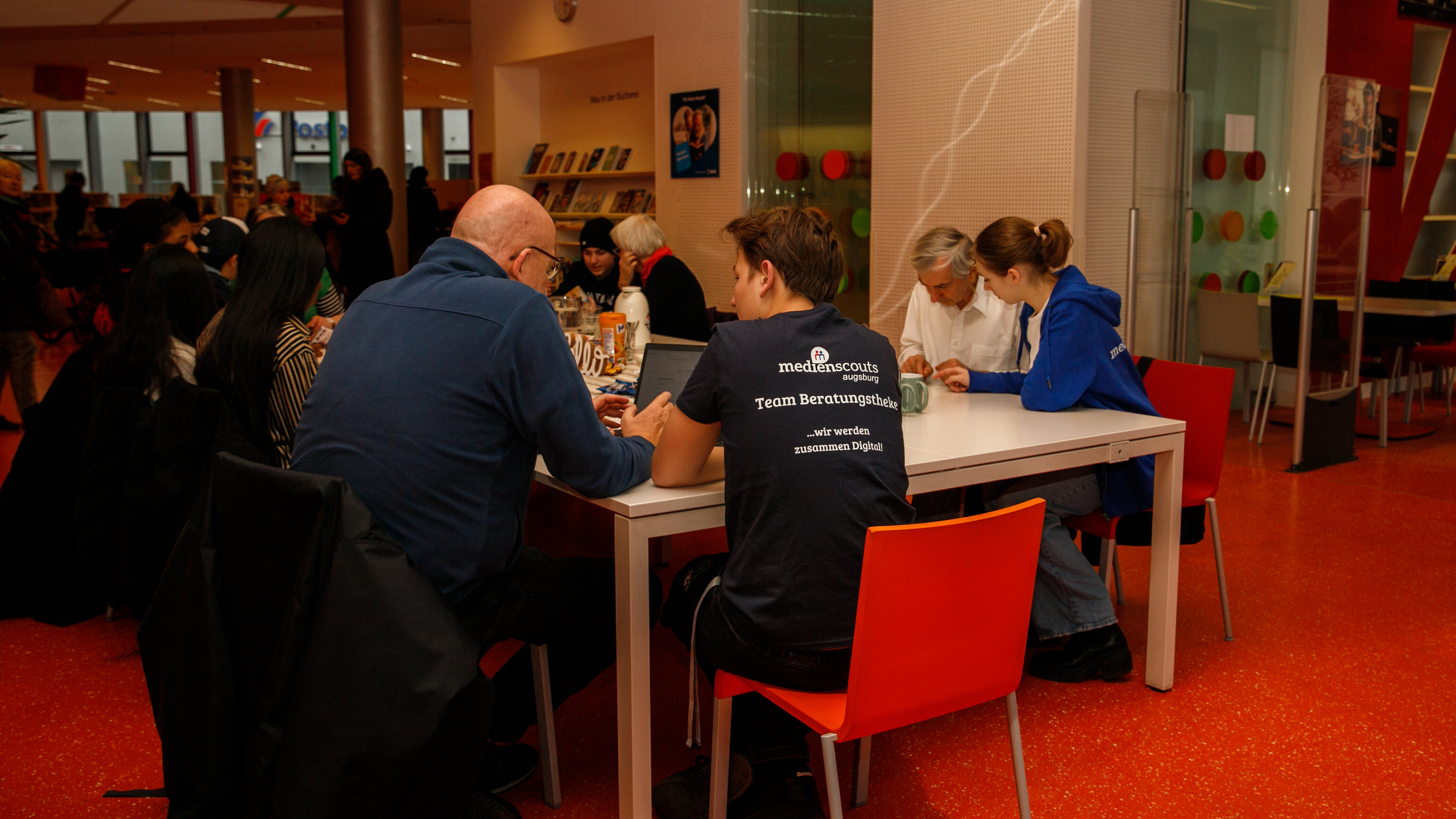 Das Foto zeigt einen älteren Mann vor einem Tablet. Neben ihm sitzt Junge, der ihm etwas erklärt. Der Junge trägt ein T-Shirt mit der Aufschrift Medienscouts