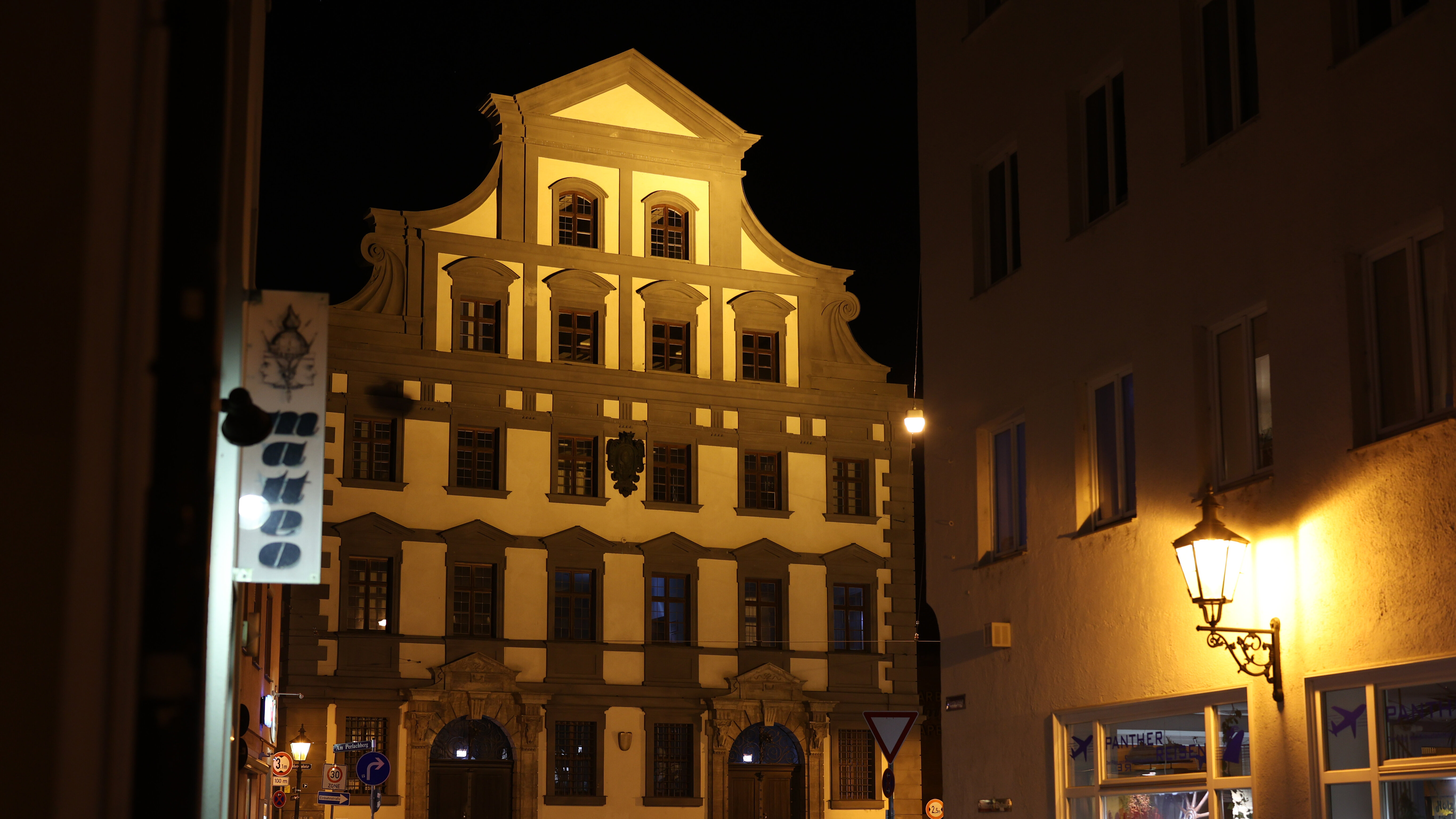 schummrig beleuchtete Fassade des Augsburger Zeughauses mit Fassadenschmuck  und Spitzgiebel