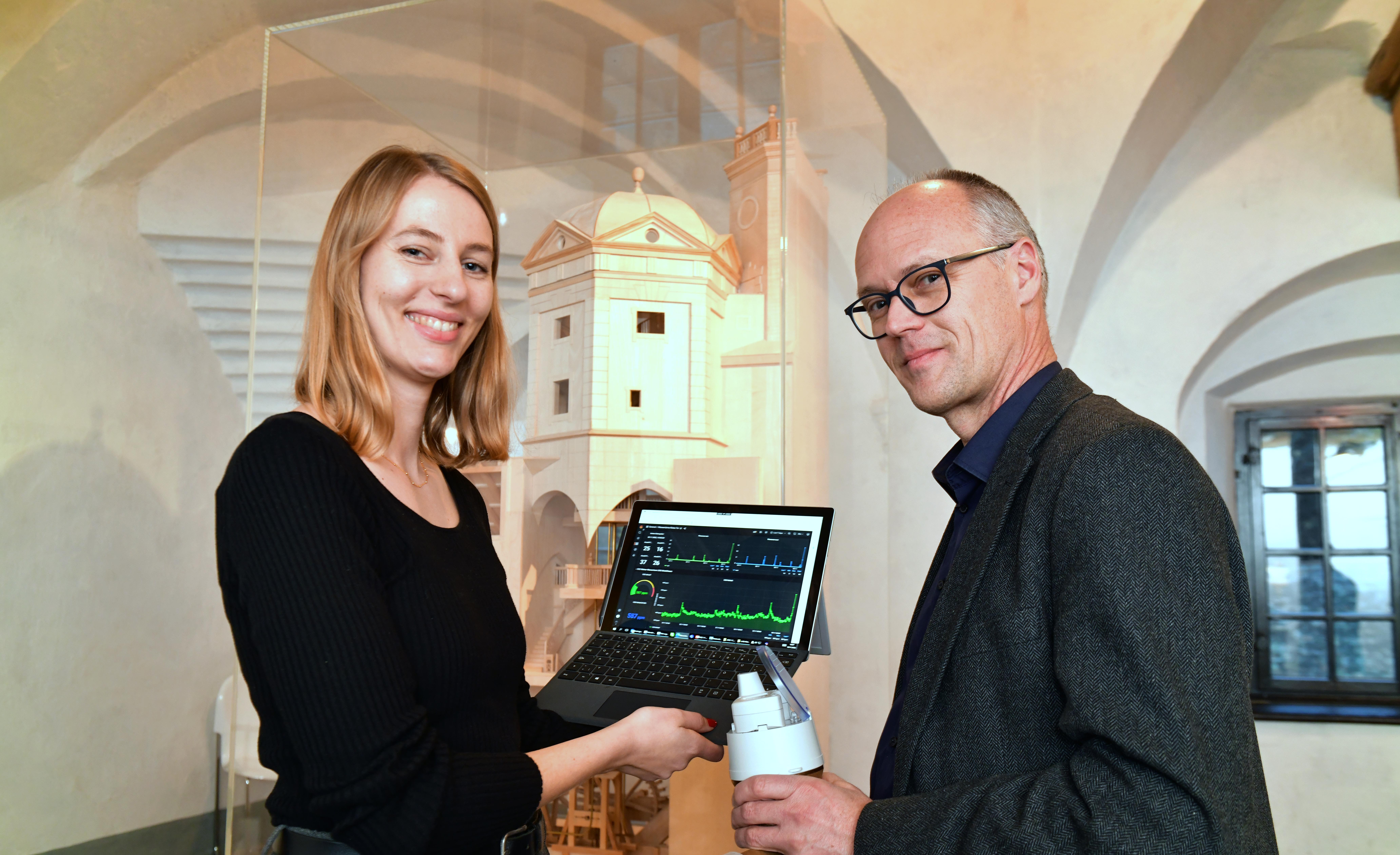 Eine Frau und ein Mann stehen mit einem Laptop in einem historischen Wasserturm. Auf dem Laptop sind verschiedene Daten zu erkennen.
