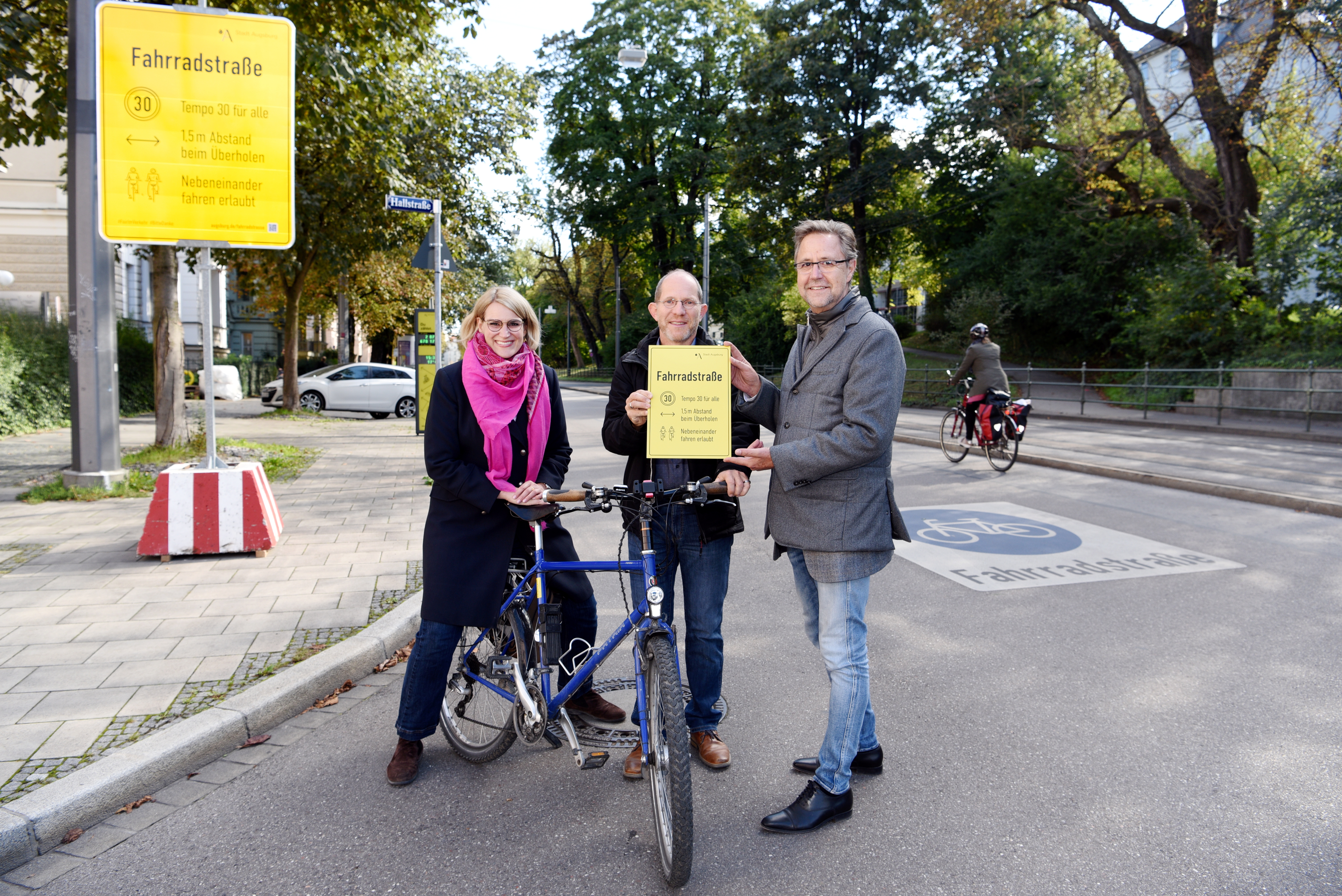 OB Eva Weber, der städtische Fahrradbeauftragte Janos Korda und Baureferent Gerd Merkle (von links) stehen mit einem Fahrrad vor einem großen gelben Schild. Das Schild zeigt die Regeln, die in einer Fahrradstraße gelten.
