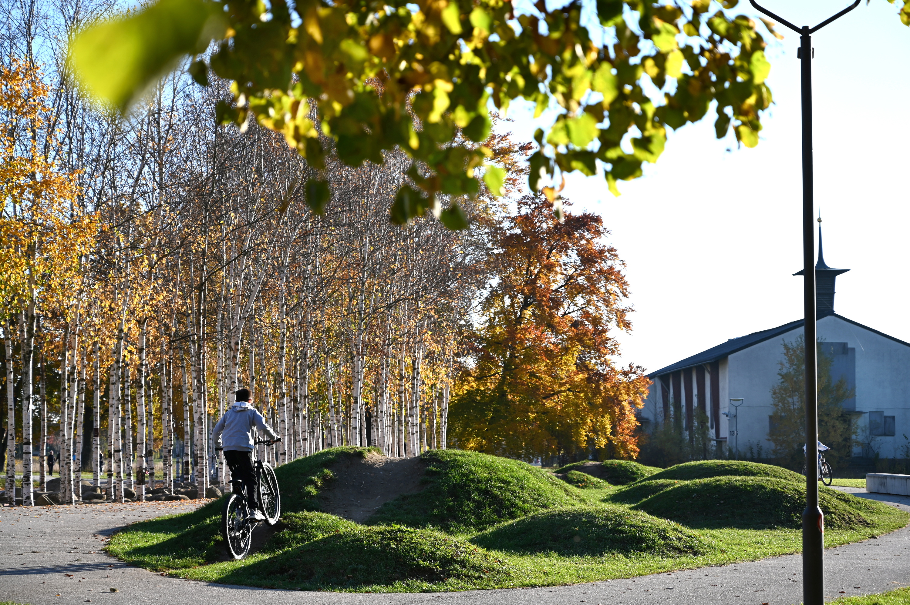 Im Westpark fahrt ein junger Radfahrer über begrünte Hügel. Im Hintergrund ist die Kapelle der früheren Kaserne zu sehen. 